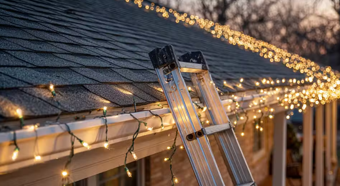 A ladder leaning against a house decorated with string lights on the roof during dusk.