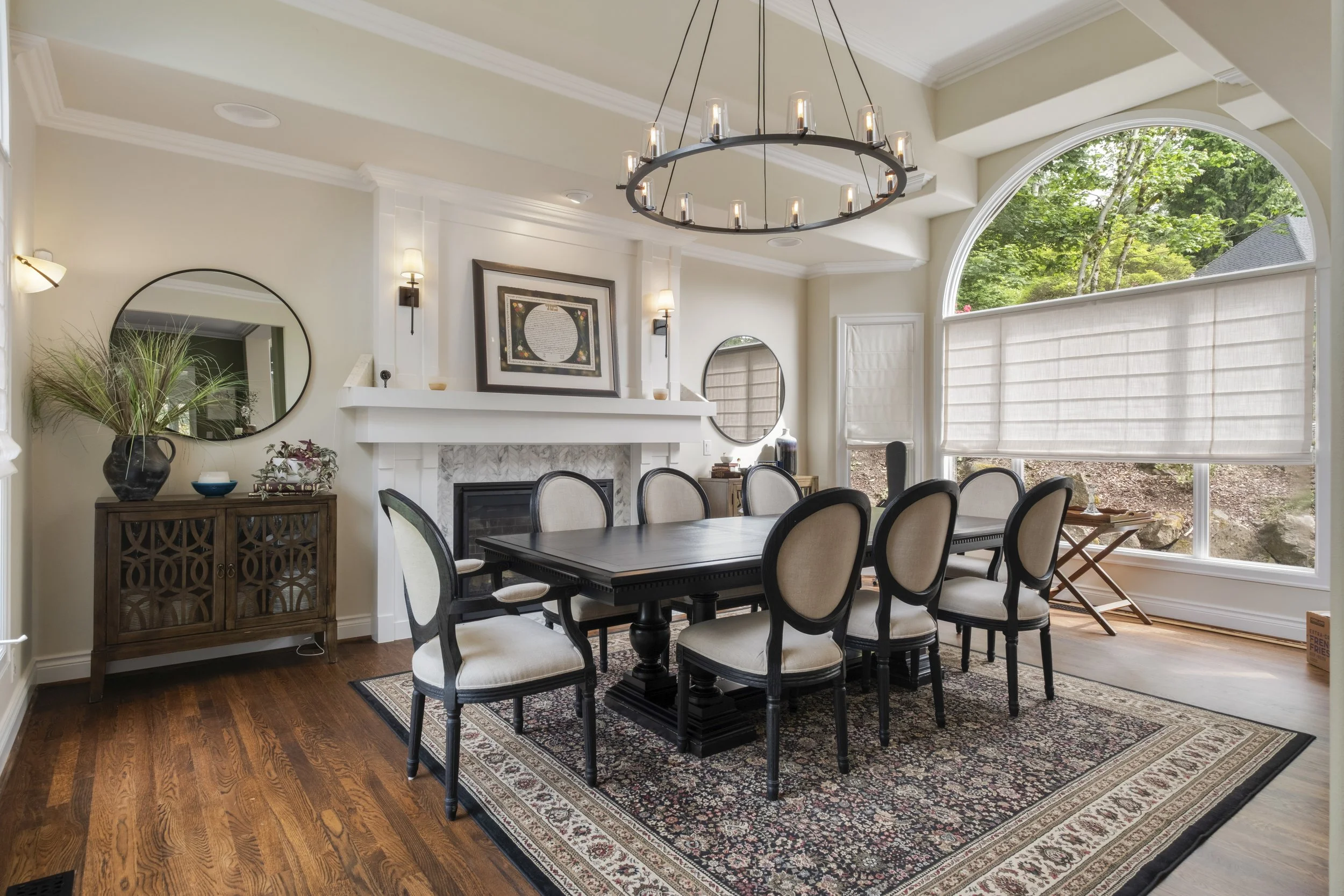 Luxury dining room remodel at the Westview Home on Mercer Island, WA, featuring a statement chandelier, custom fireplace surround, crown molding, hardwood flooring, and expansive arched windows completed by F&M Construction & Remodeling.