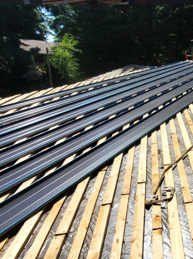 Solar panels installed on a rooftop with wooden planks and roofing materials underneath, surrounded by trees in a residential neighborhood.