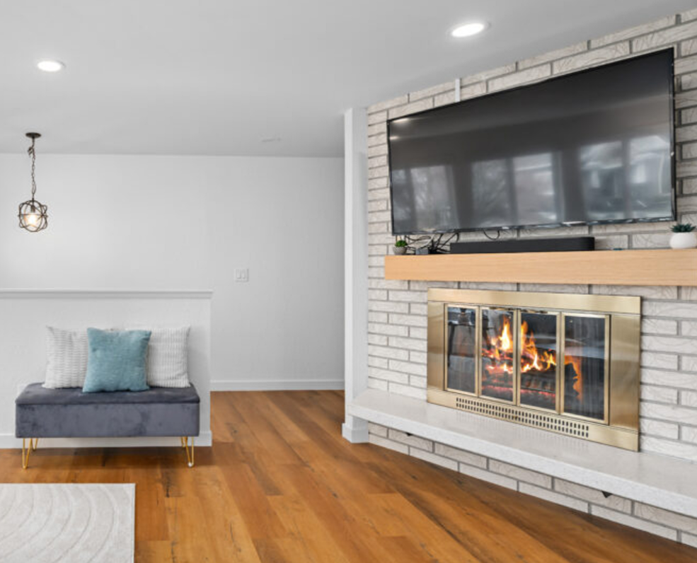 White brick fireplace installation completed by F&M Construction & Remodeling in Seattle, WA, featuring a custom fireplace surround, wood mantel, built-in television, and luxury living room remodeling for Eastside homes.