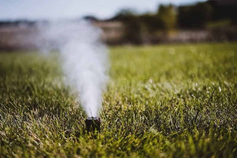 A sprinkler releasing water into a grassy field on a sunny day.
