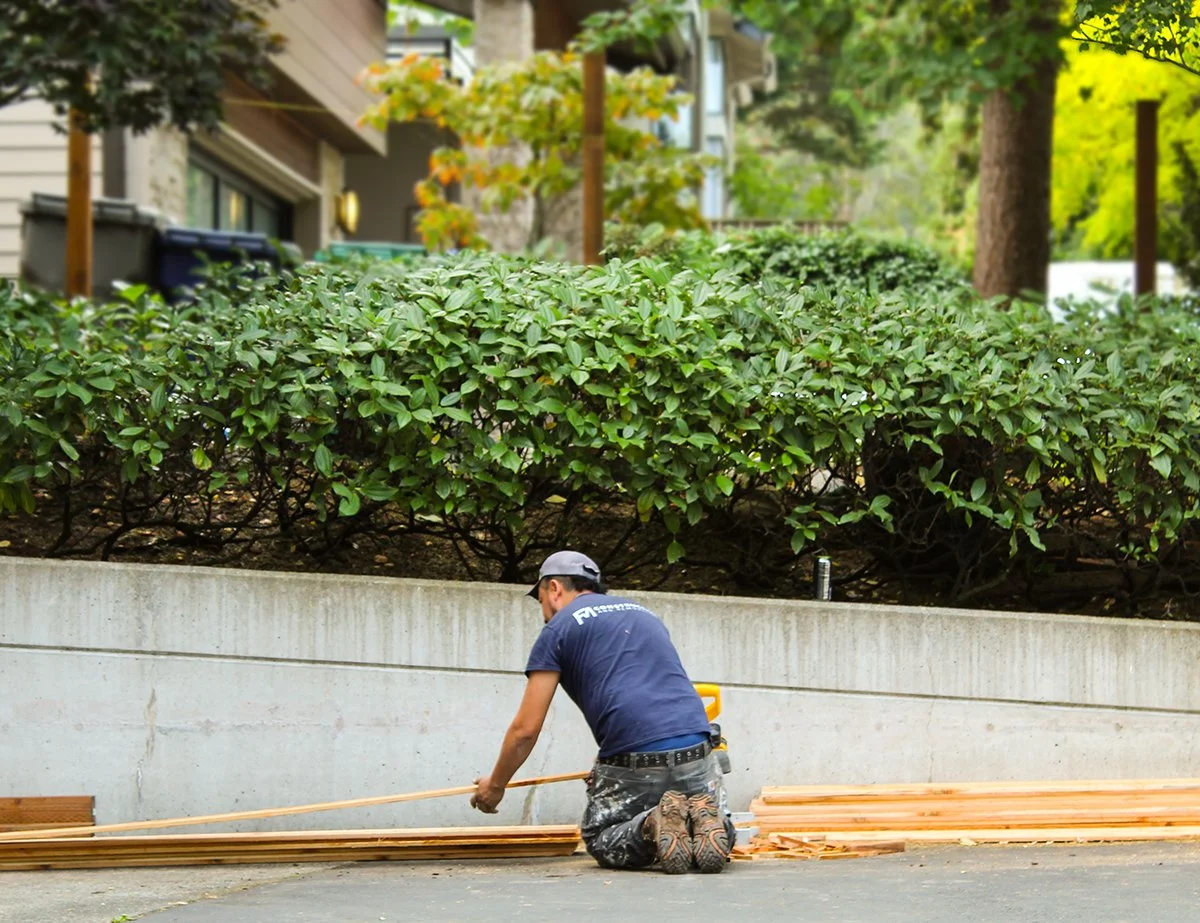 A man kneeling on the ground and working with wooden planks outdoors.