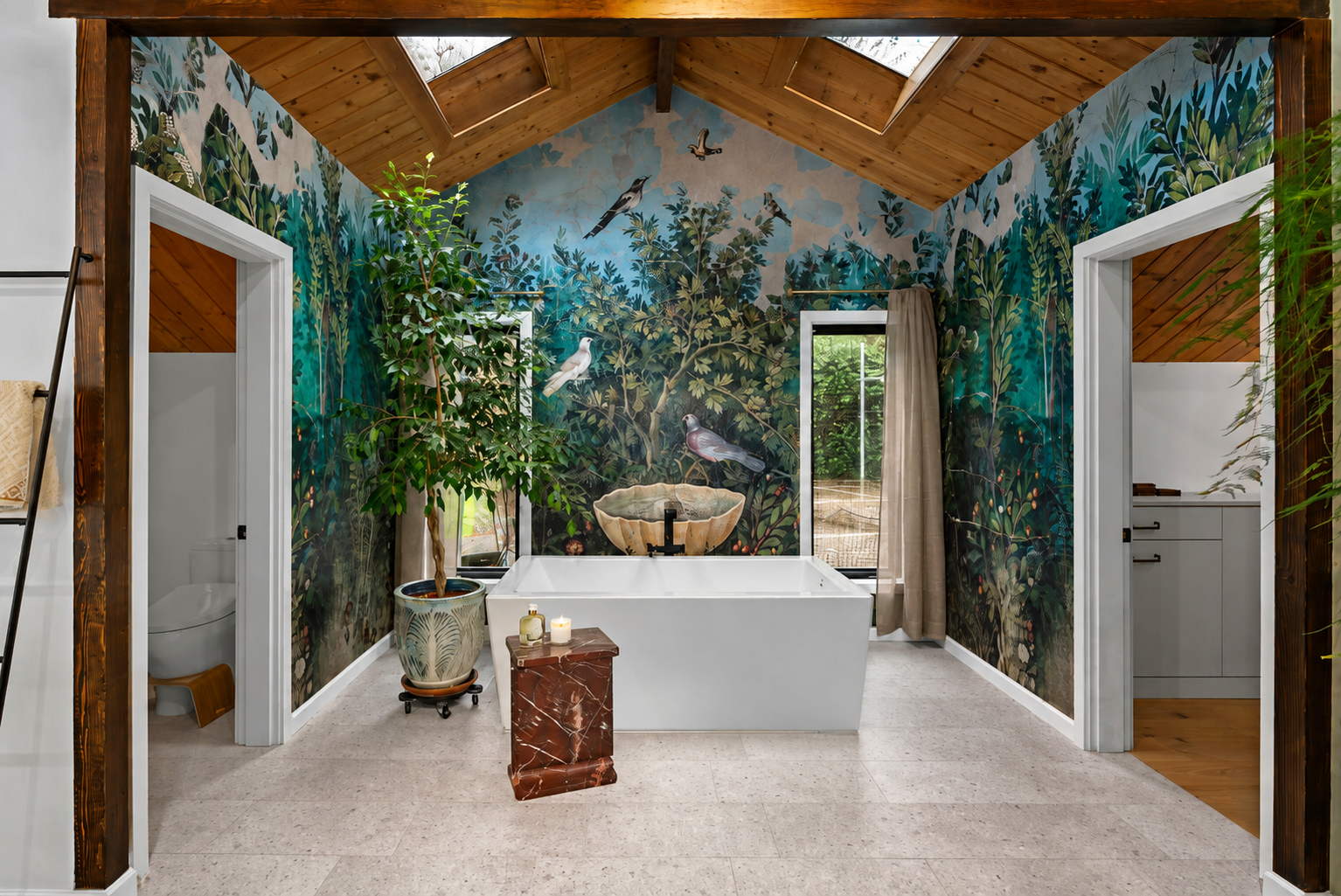 A bathroom with nature-inspired wallpaper featuring birds and foliage, a white bathtub, a small side table with candles, a large potted plant, ceiling skylights, and a window with a curtain.