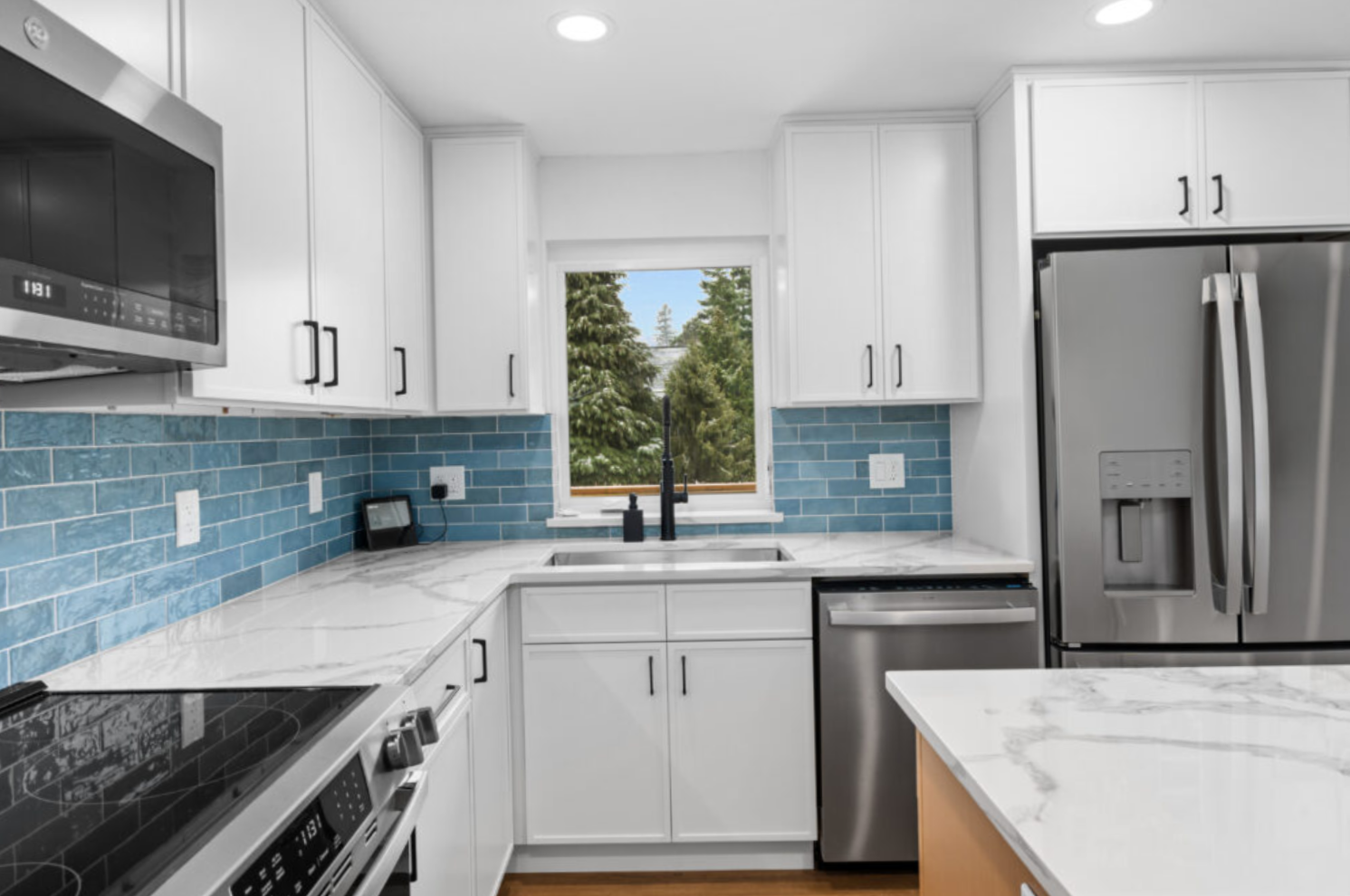 Modern kitchen remodel at the Allison Home in Seattle, WA, featuring white shaker cabinets, quartz countertops, blue subway tile backsplash, stainless steel appliances, and a large island completed by F&M Construction & Remodeling.