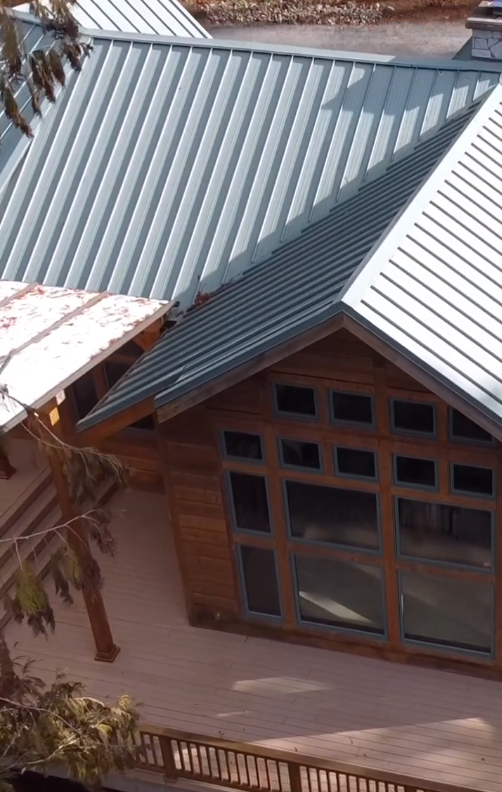 Aerial view of a house with a metal roof and large windows, wooden siding, and a small wooden deck.