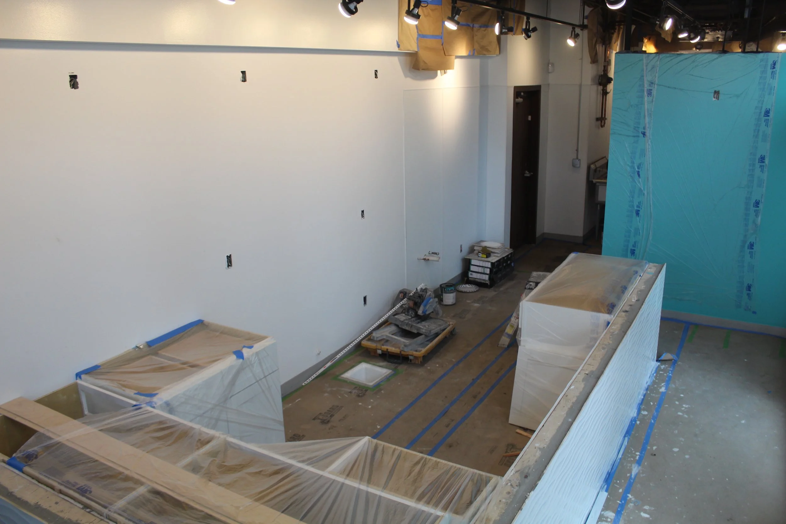 Just Poke indoor construction site with partially finished walls, covered furniture, and construction tools and materials on the floor, with track lighting installed overhead.