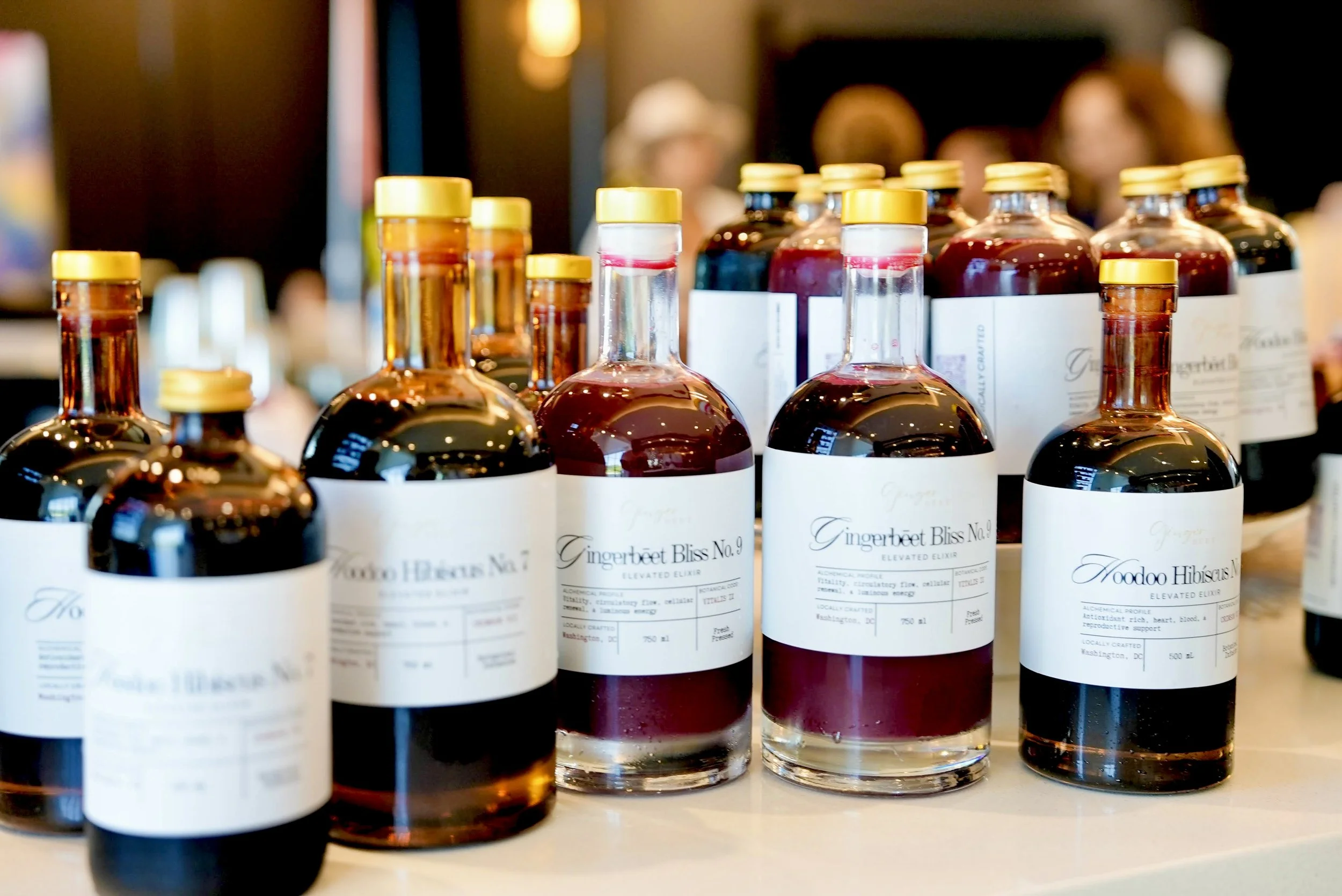 A display of Ritūal Réserve non alcoholic elevated elixirs labeled as botanical elixirs, with white labels and gold caps, placed on a surface in Aston Martin at the bar with plant-based cuisine at a luxury wellness event,