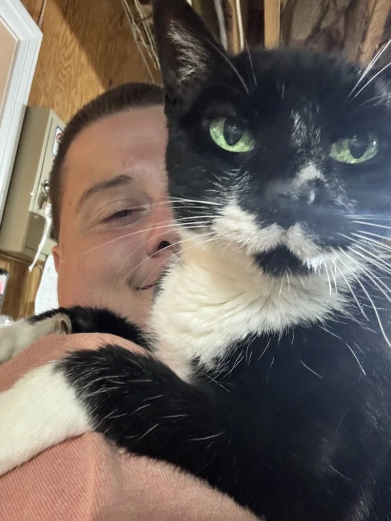 A person holding a black and white cat close to their face, with the person's face partially visible and the cat looking directly at the camera.