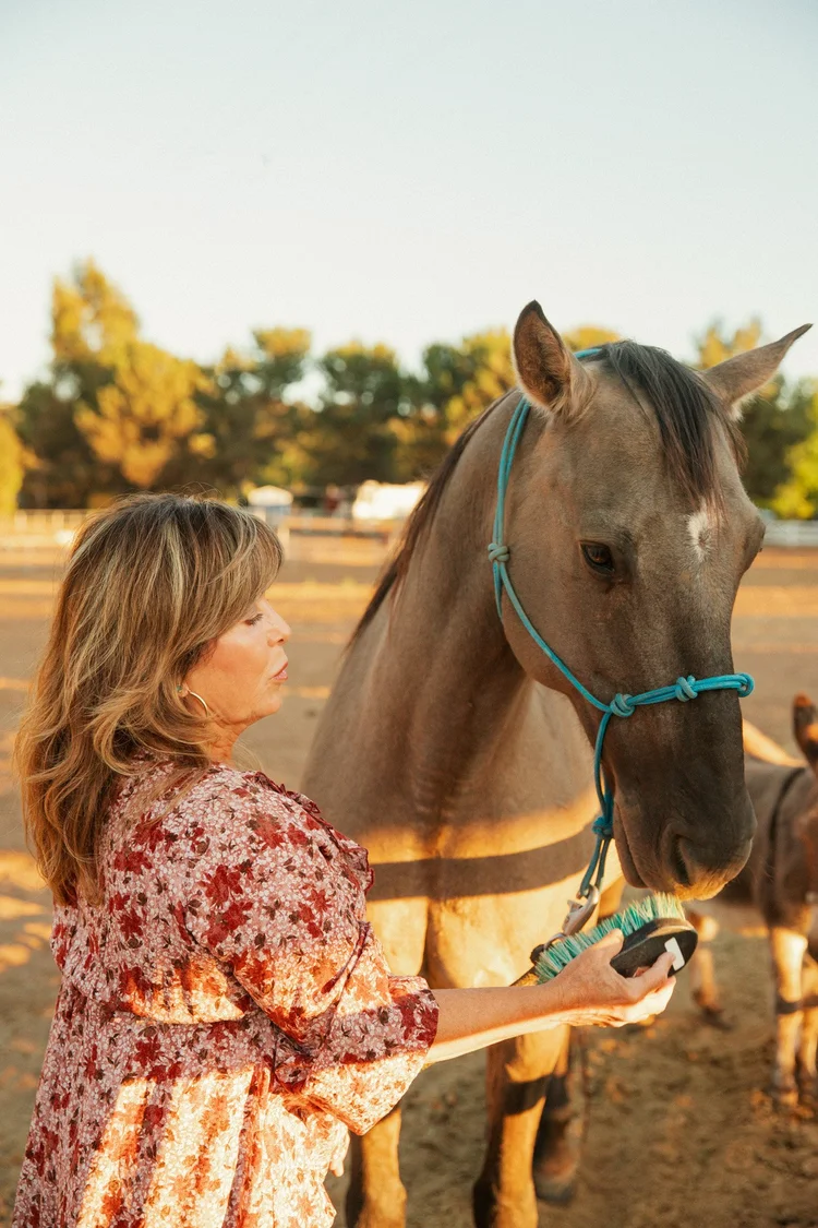 A woman in a floral blouse standing with her horse in warm evening light