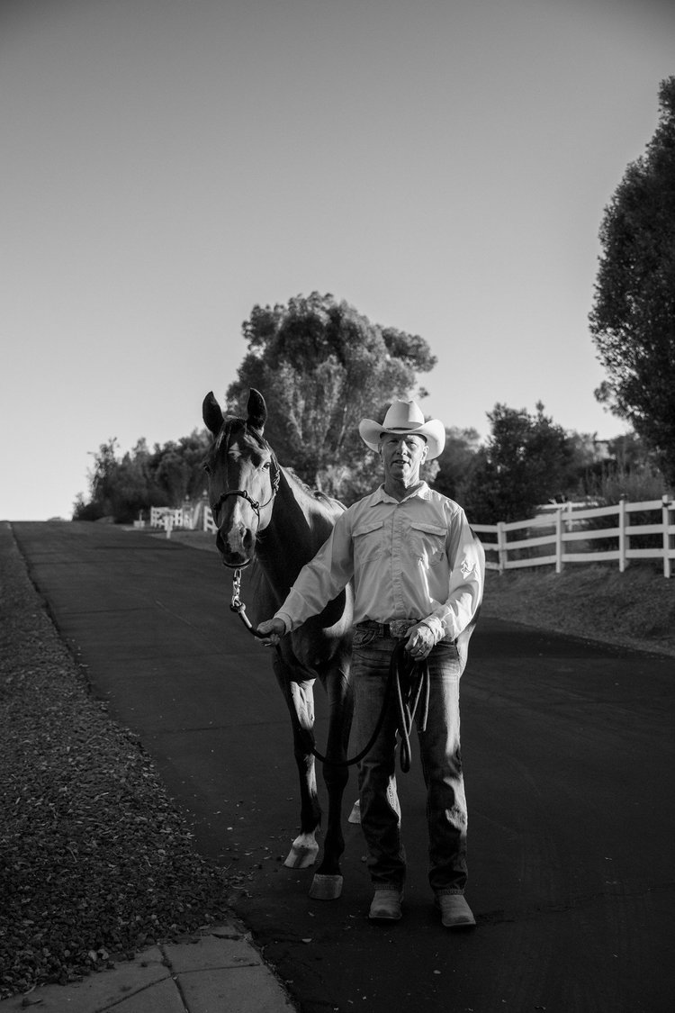 Black and white photograph of two people with a horse on a ranch road