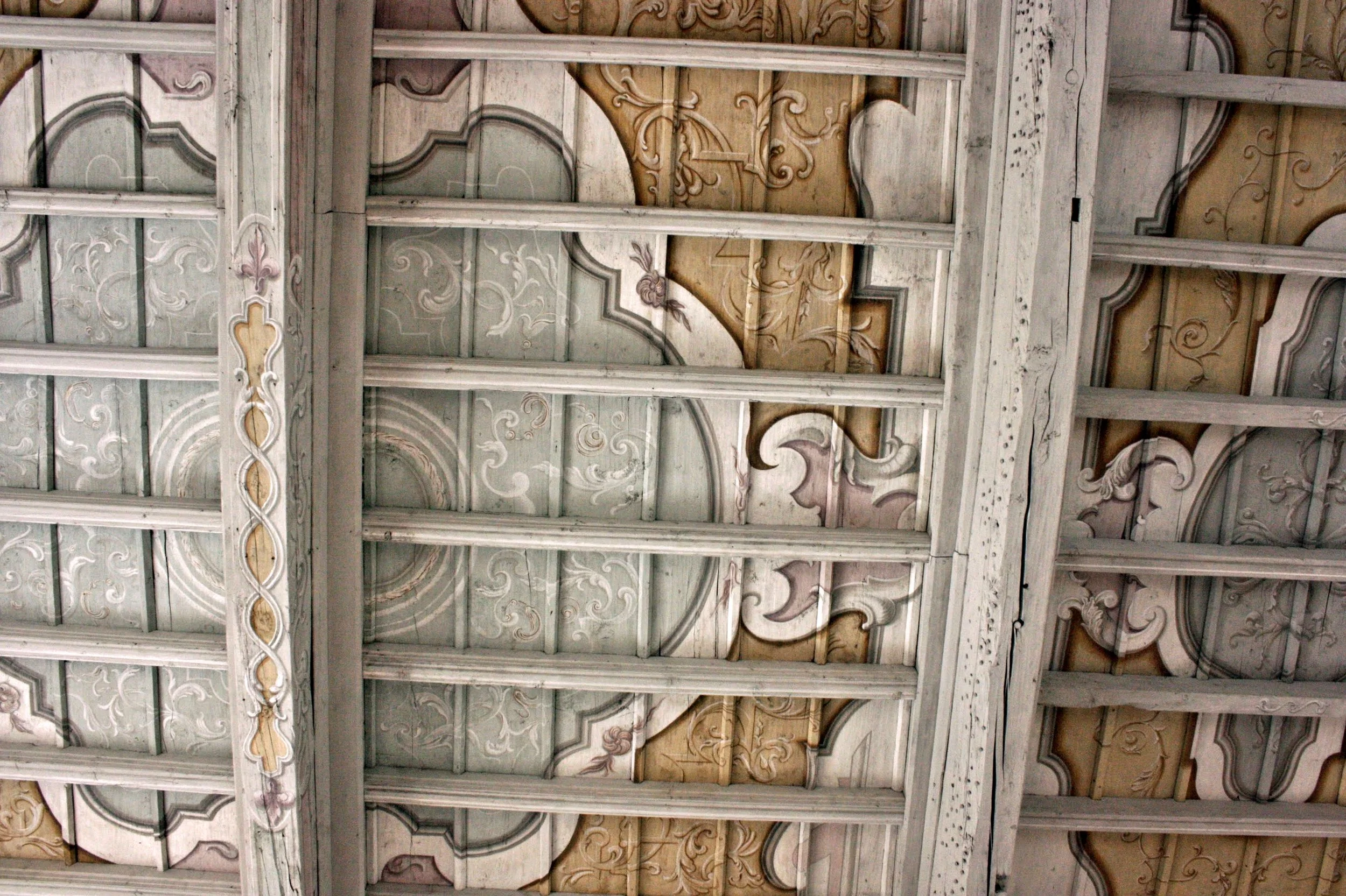 Soffitto in legno decorato con motivi floreali e volute ornamentali in tonalità delicate.