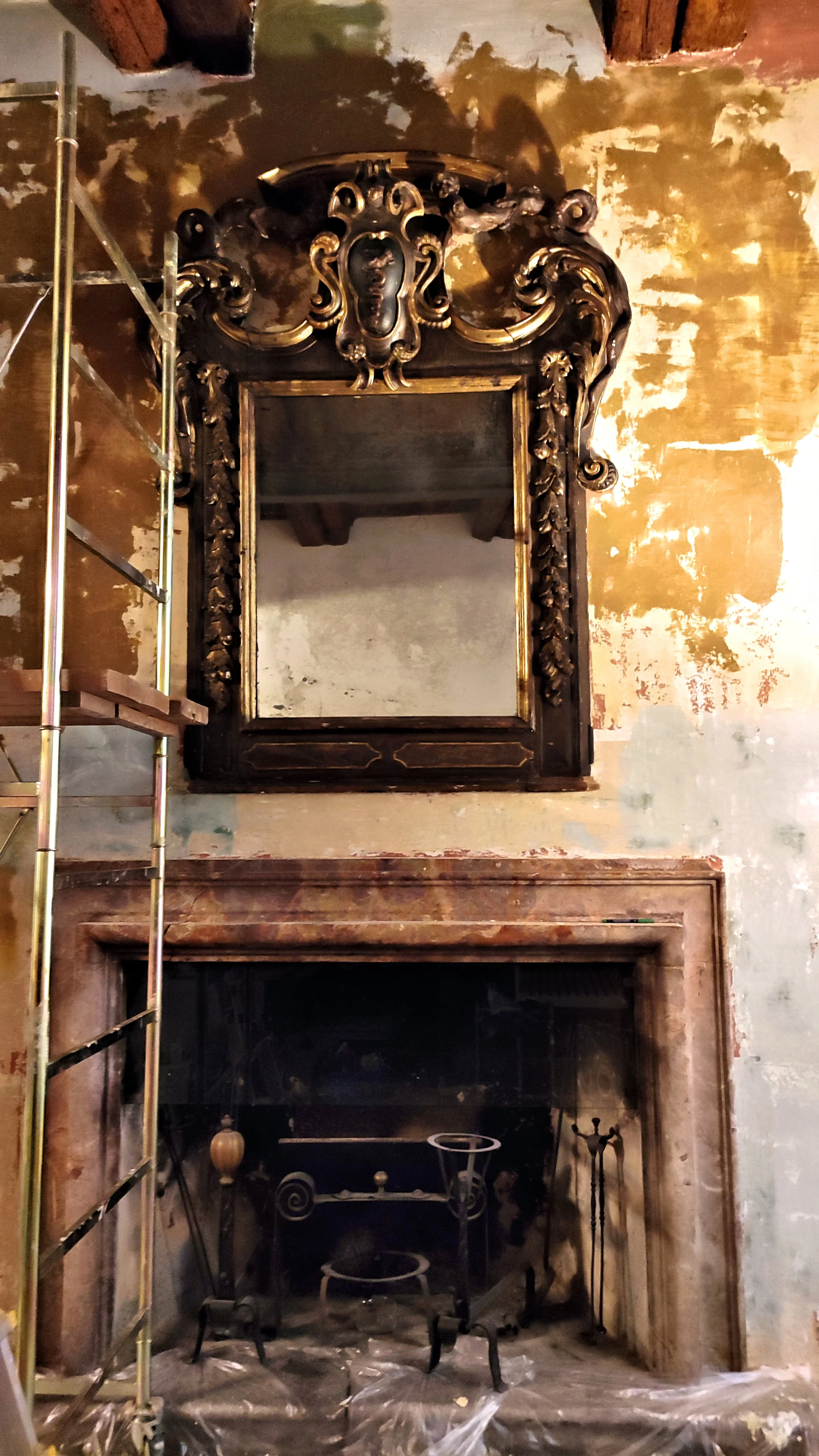 Specchio antico decorato sopra un camino, con parete a finitura delabré durante i lavori di recupero.