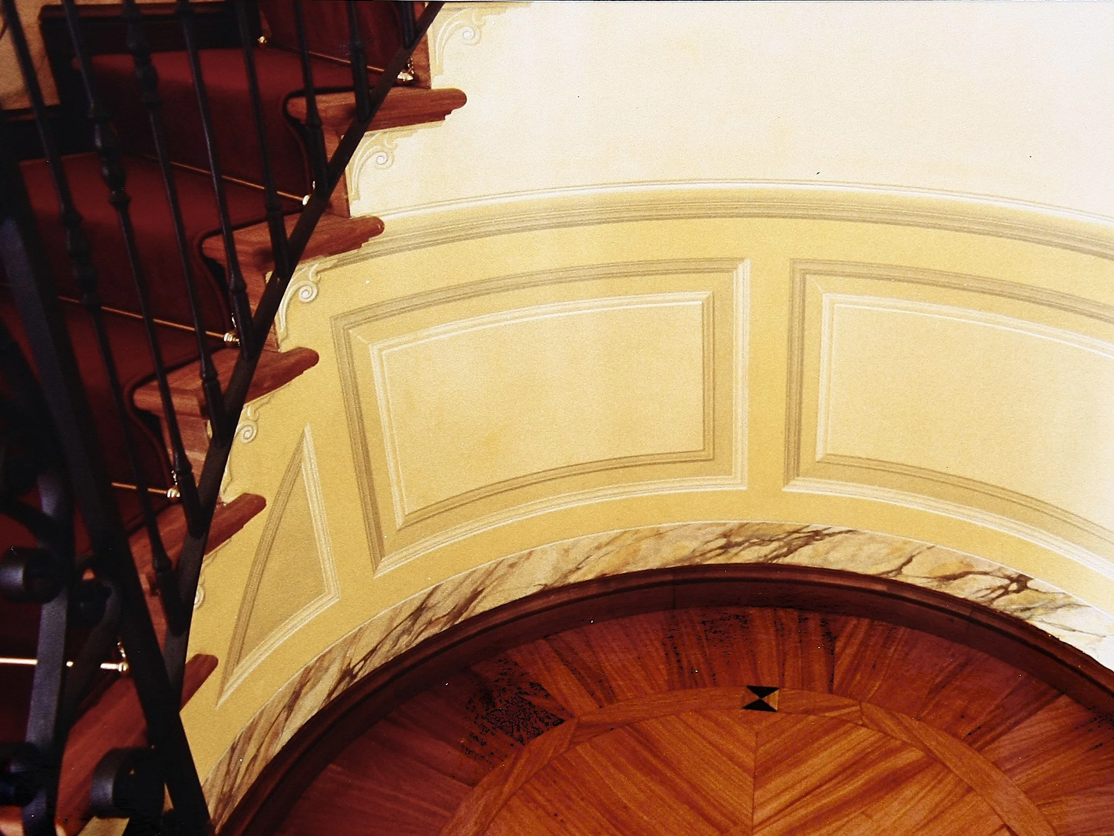 Scala con gradini in legno, ringhiera nera e pareti decorate con boiserie.