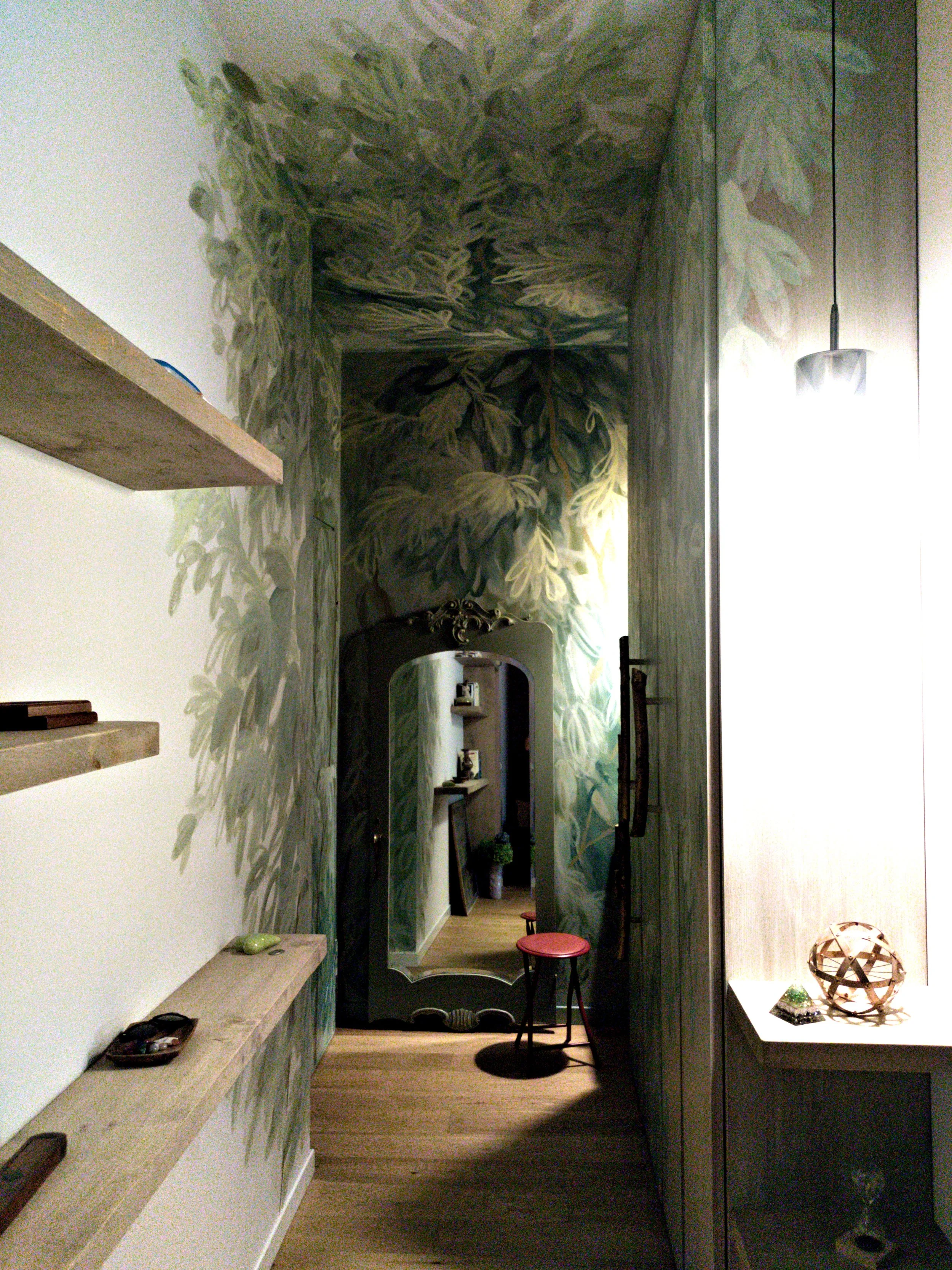 Ingresso finito con pareti decorate da un motivo floreale scuro, specchio, mensole e complementi d'arredo.