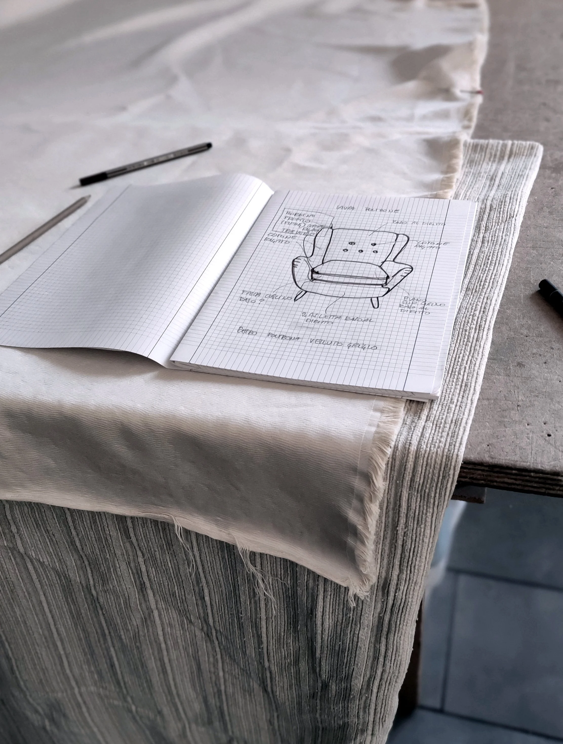 Sketch of a chair with labels and notes on graph paper, placed on a striped cloth and a textured surface.