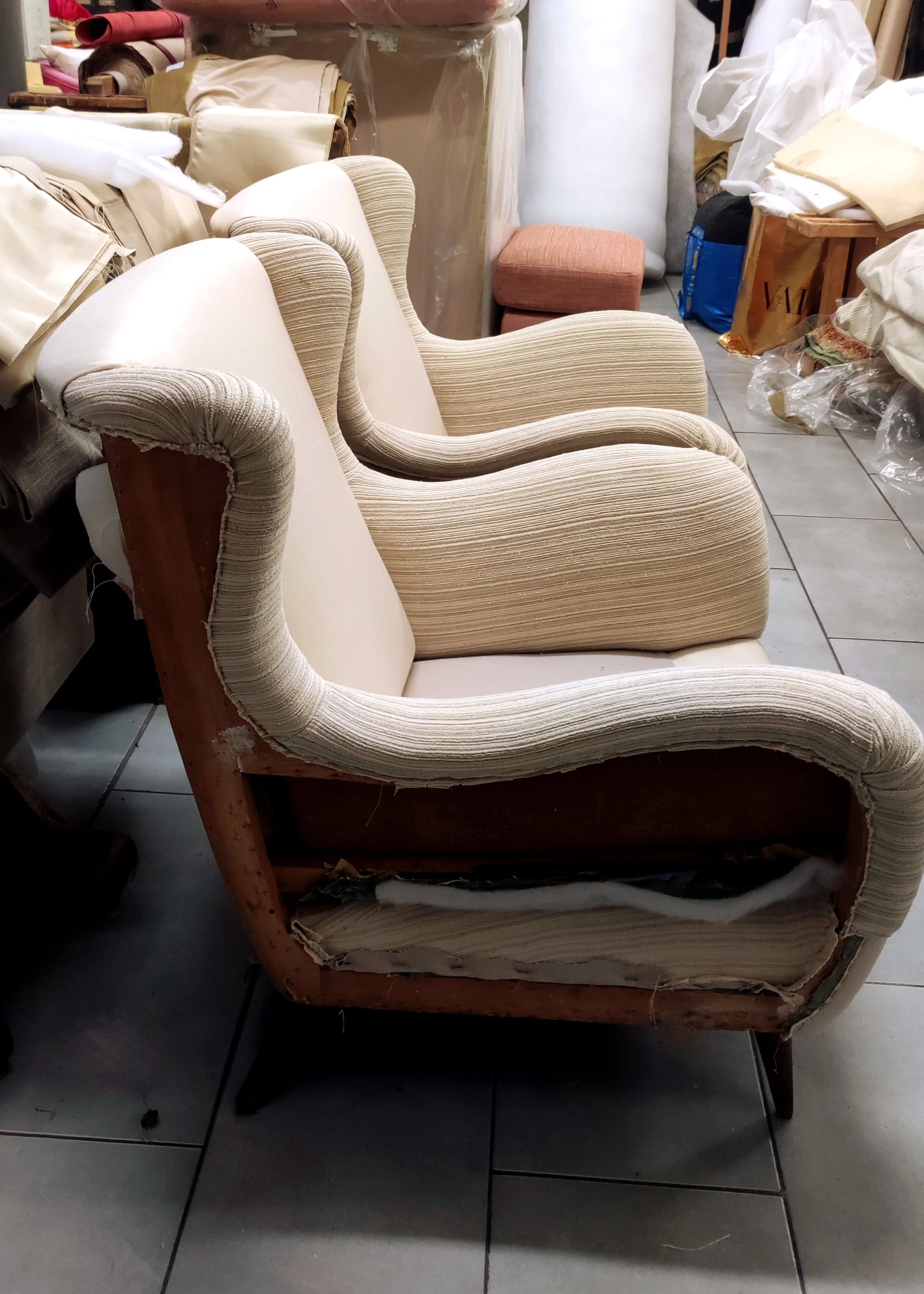 An old, partially disassembled wooden armchair with cushioned upholstery in a cluttered storage area.
