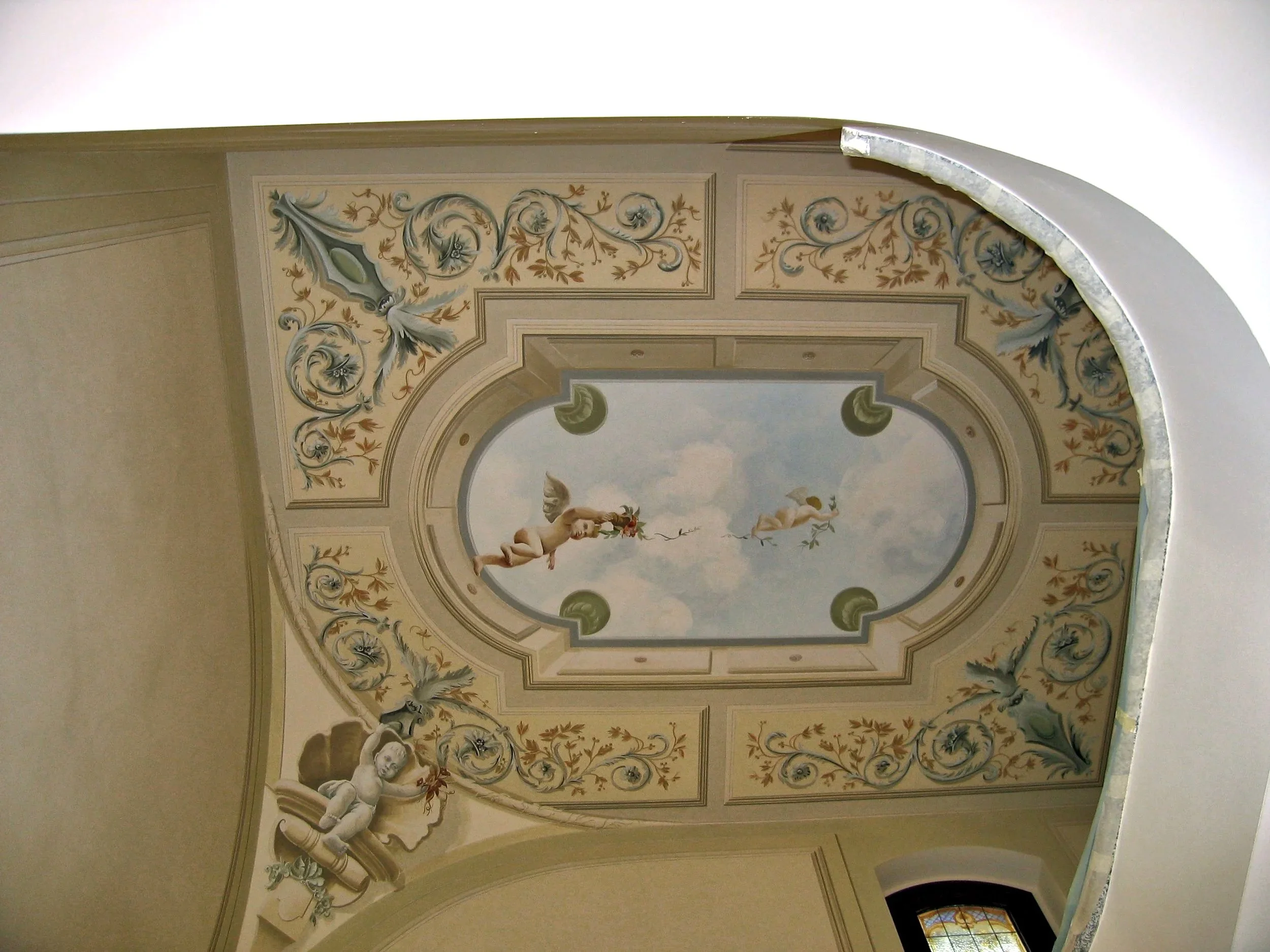 Soffitto decorato con pittura murale raffigurante putti, motivi floreali e decorazioni ornamentali.
