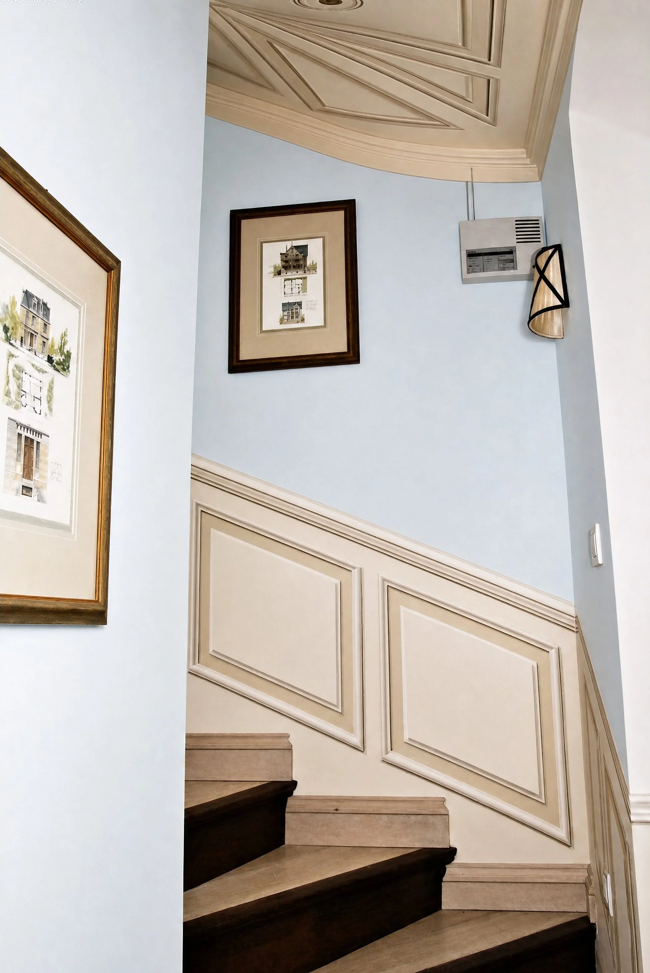 Scala con gradini in legno, pareti azzurre e boiserie decorativa nei toni del beige.