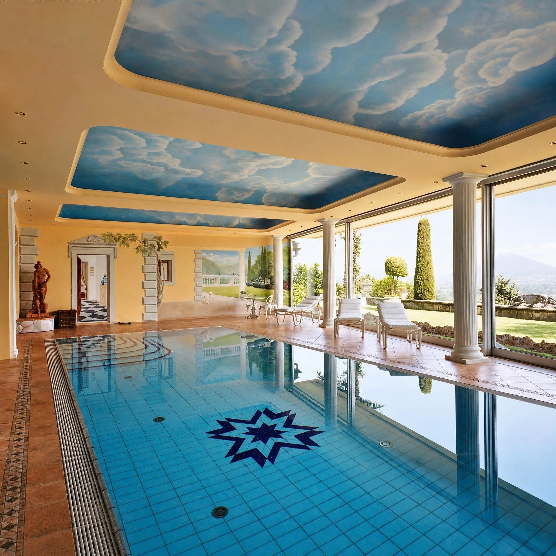 Piscina interna con piastrelle blu e soffitto dipinto come un cielo azzurro con nuvole.
