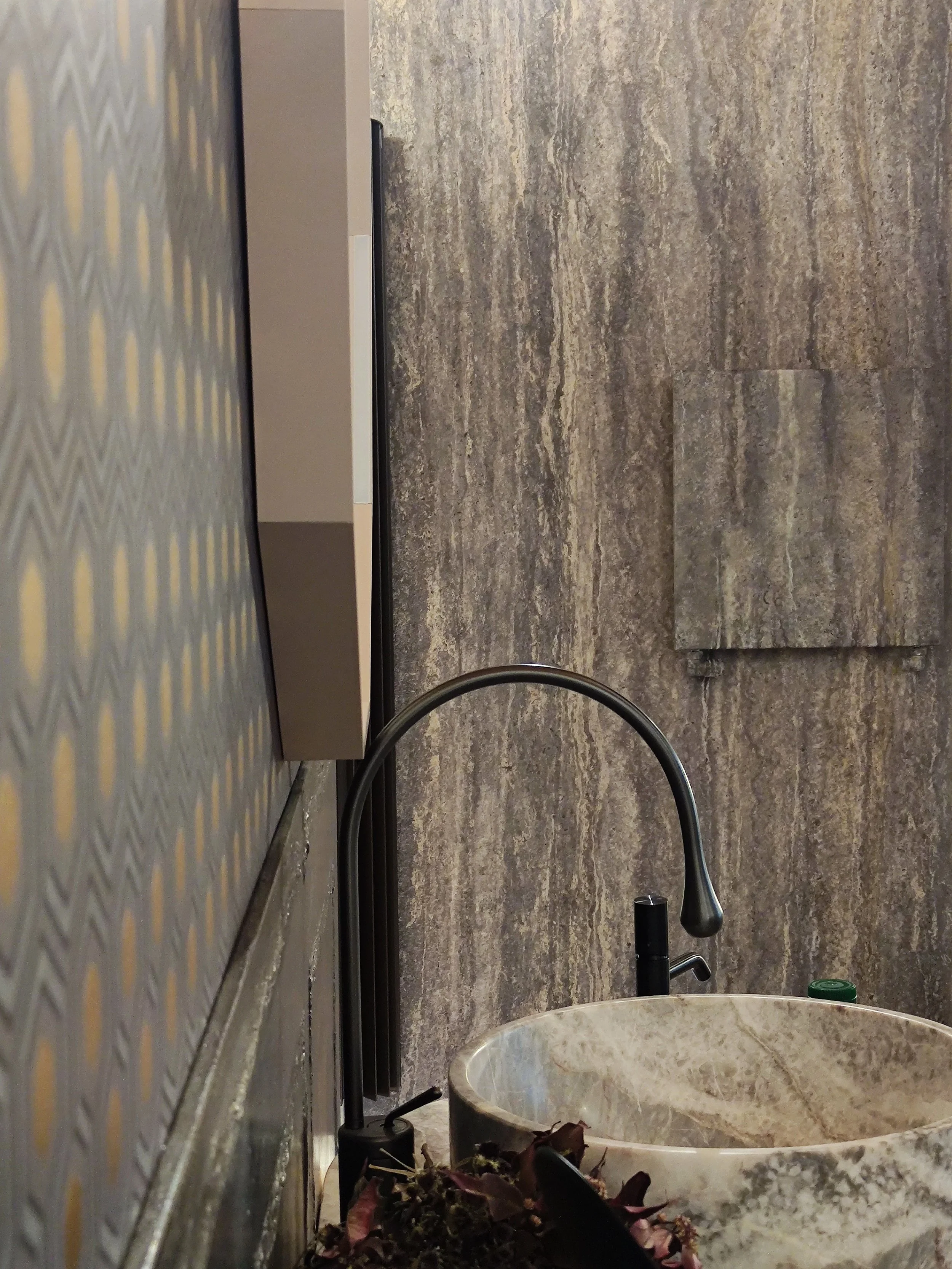 Ambiente cucina con lavello nero, rubinetto scuro e piano di lavoro in marmo decorato con elementi naturali.
