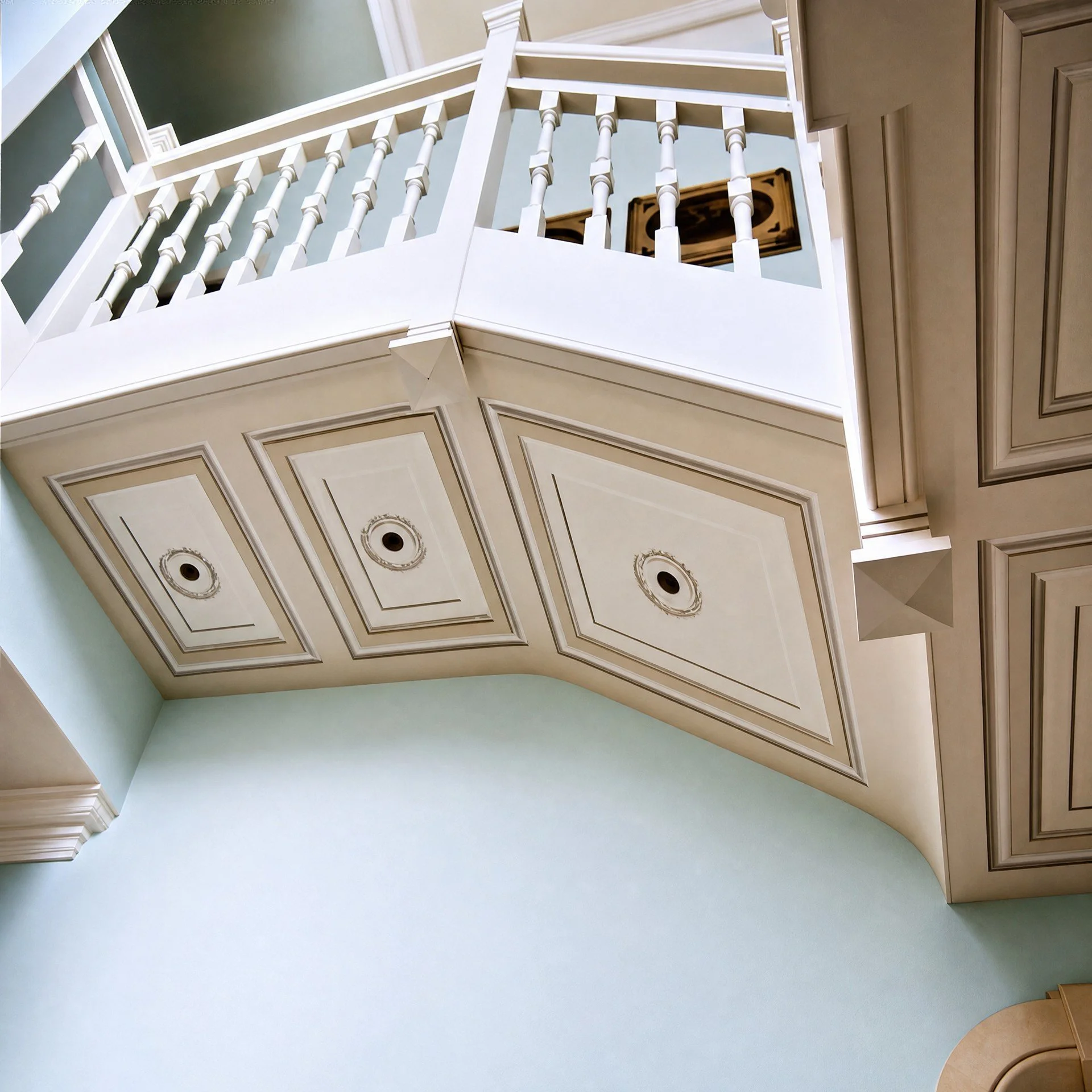 Ambiente a doppia altezza con balcone, ringhiera bianca e pannellature decorative dipinte in tonalità pastello.