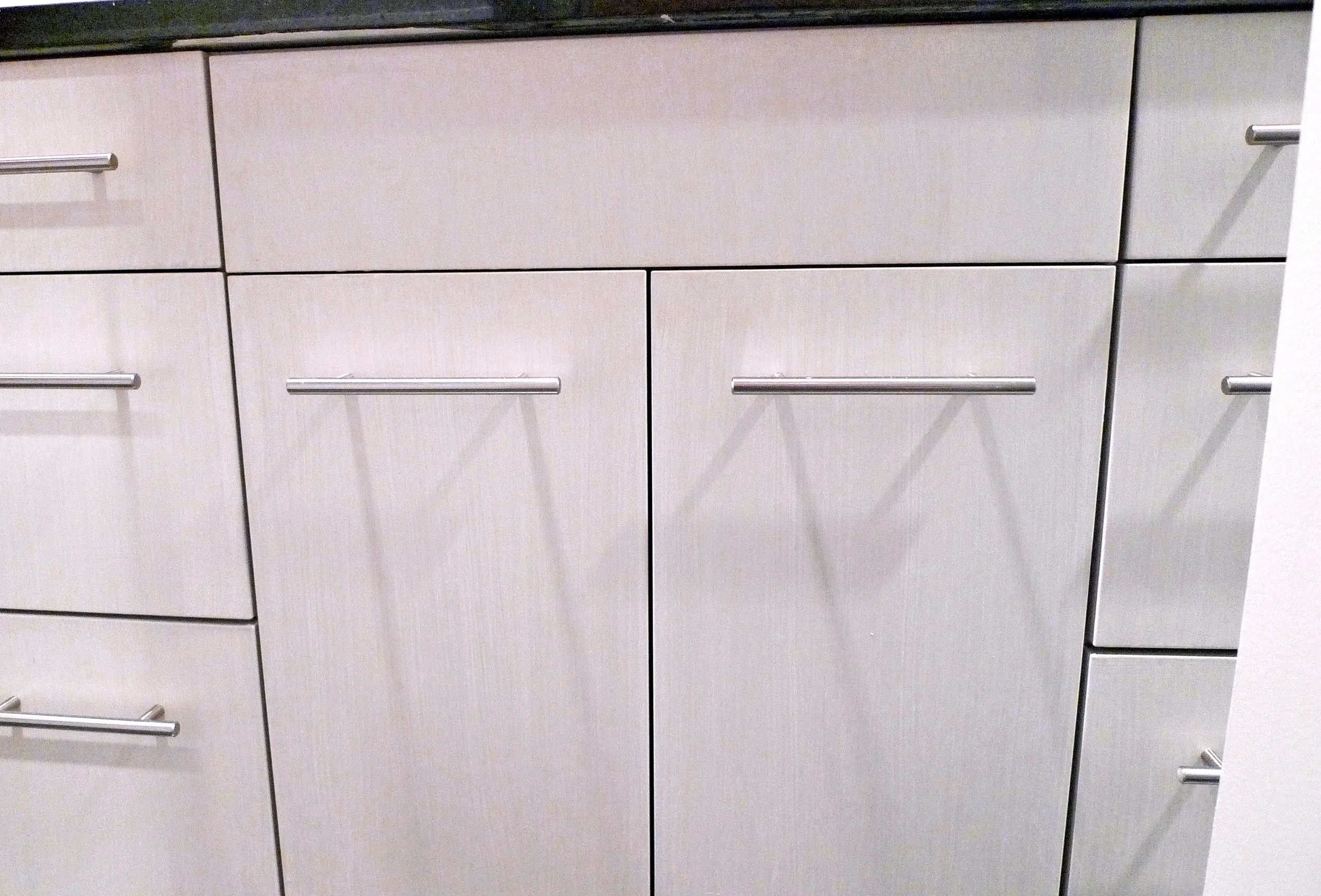 Dettaglio di mobili da cucina beige con maniglie orizzontali in metallo.