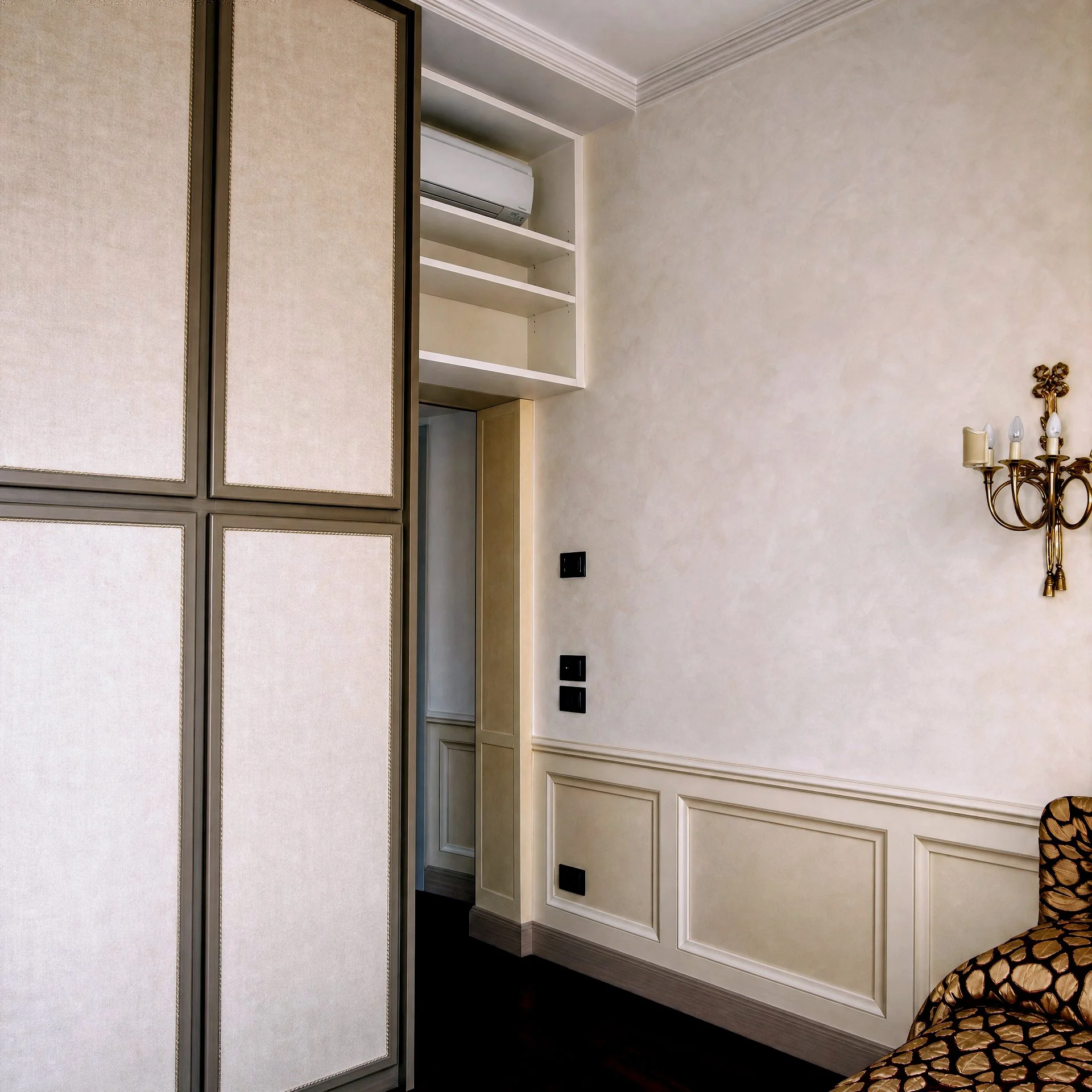 Ambiente con pareti beige, modanature decorative, mensole integrate e lampadario.