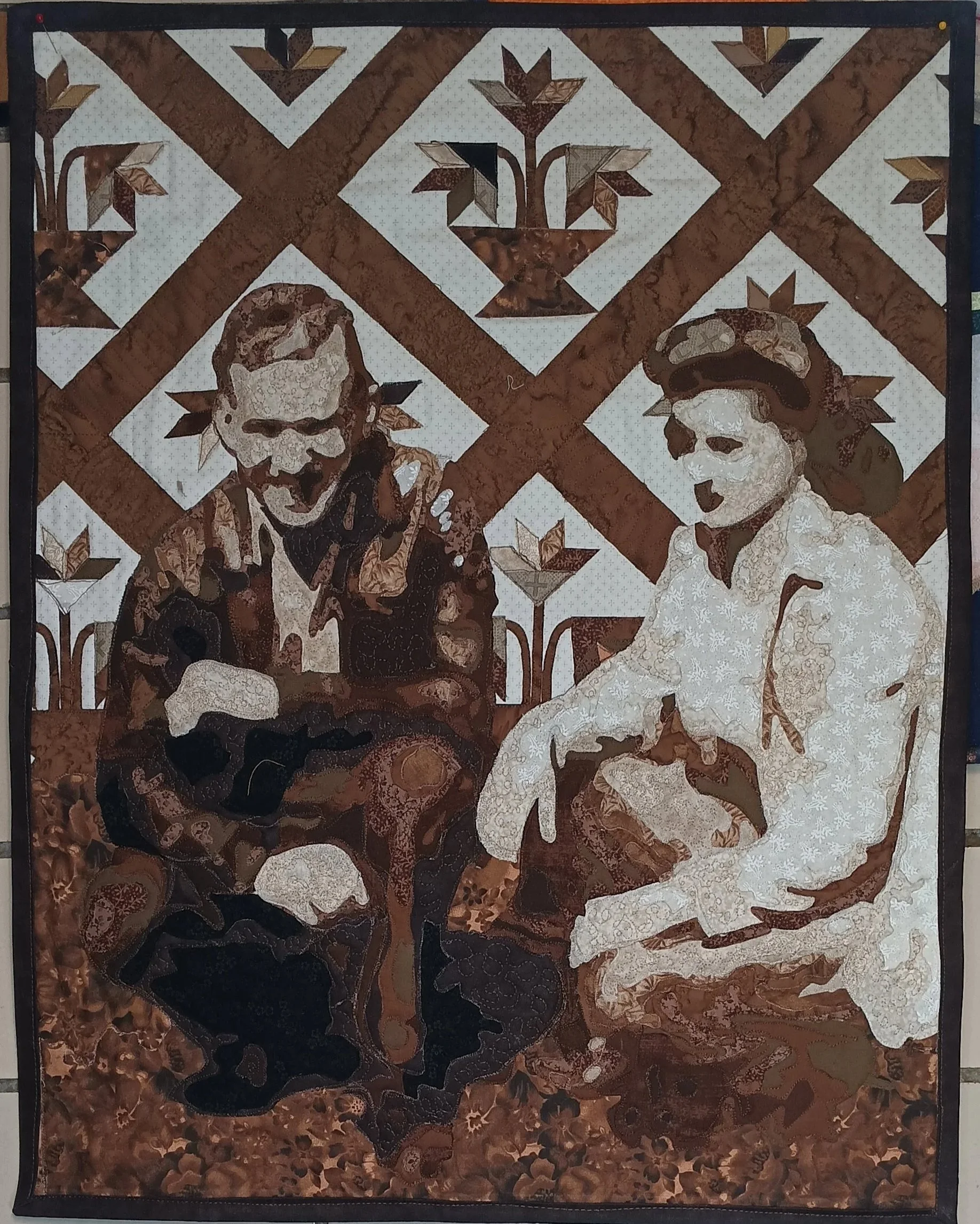 A quilted wall hanging featuring a man and woman, with a background of geometric patterns and floral motifs in shades of brown, white, and tan.