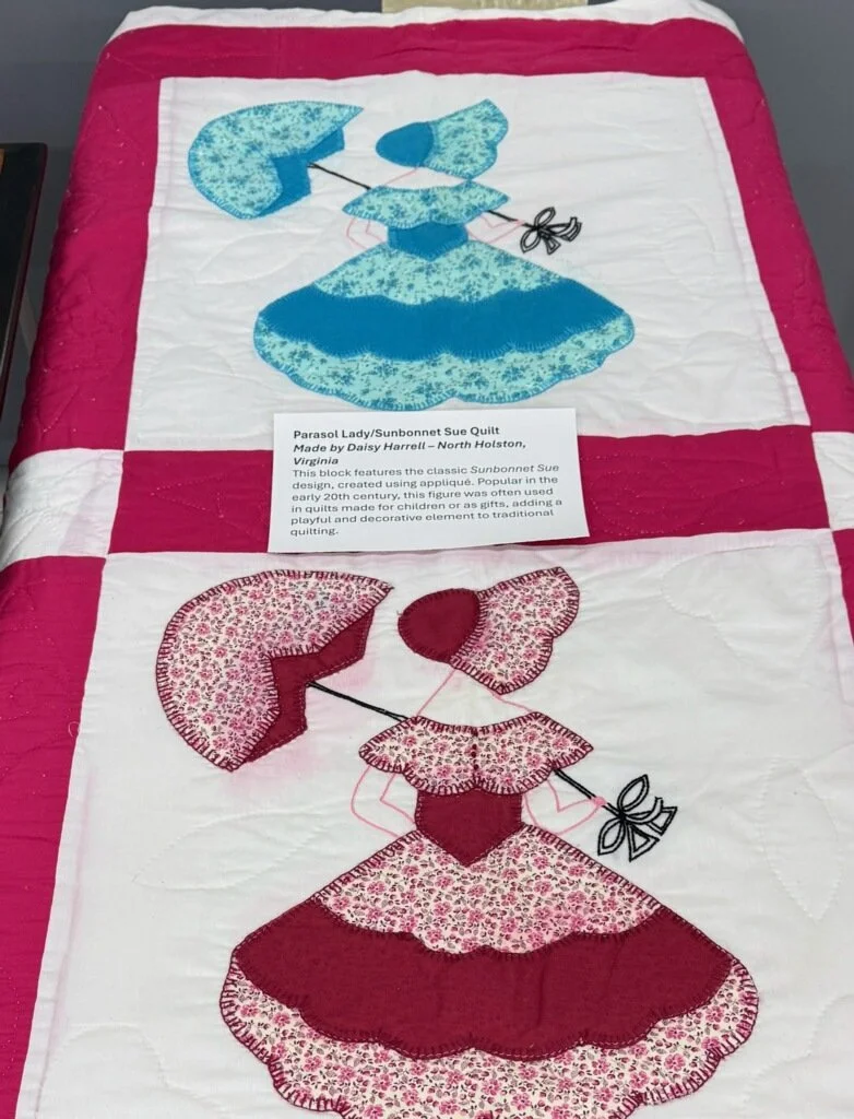 A quilt featuring two sunbonnet lady designs, one in blue and one in red, each holding a parasol.