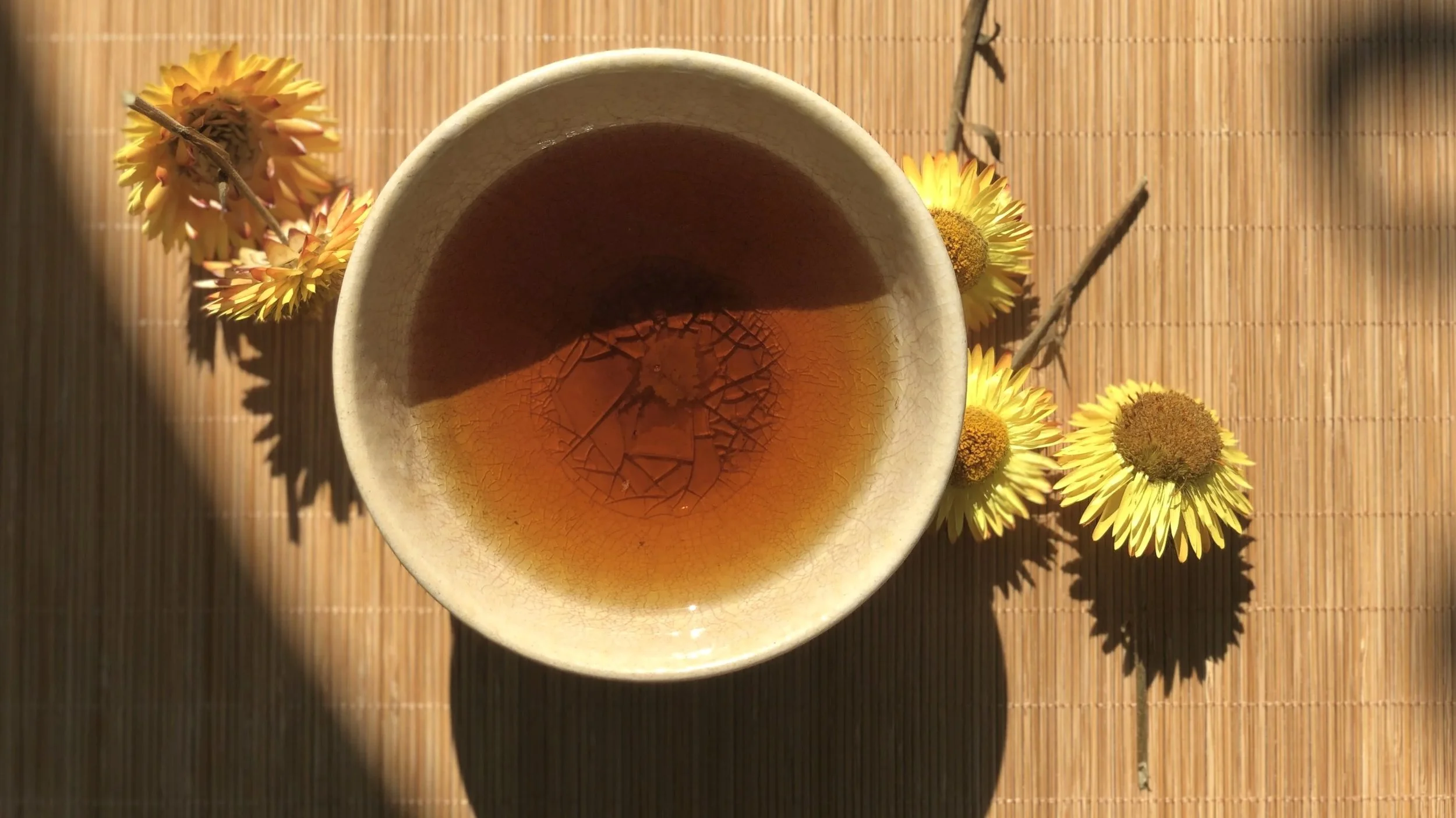 A cup of tea on a bamboo mat, with three yellow flowers around it.