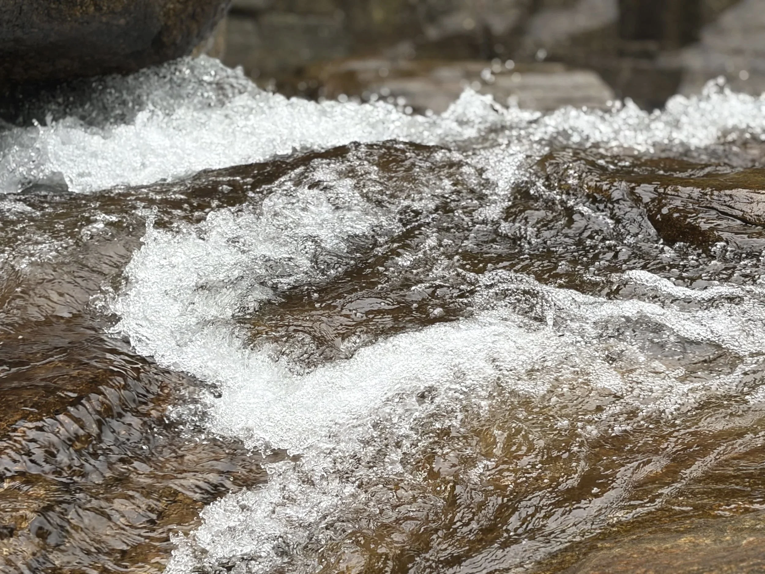 Close-up view of water flowing over rocks in a stream, with splashes and bubbles.
