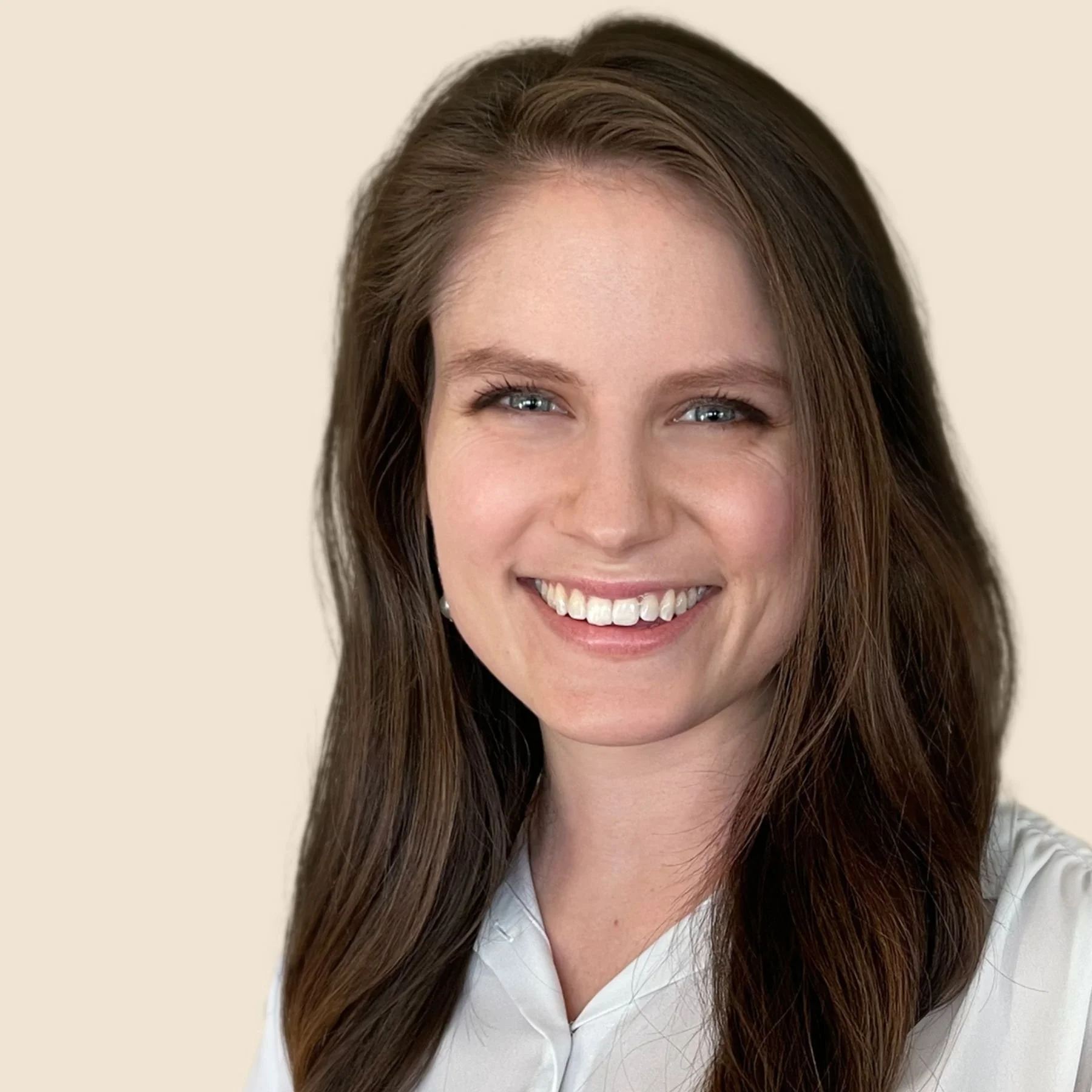 A woman with long brown hair and blue eyes smiling, wearing a light-colored shirt, against a beige background.
