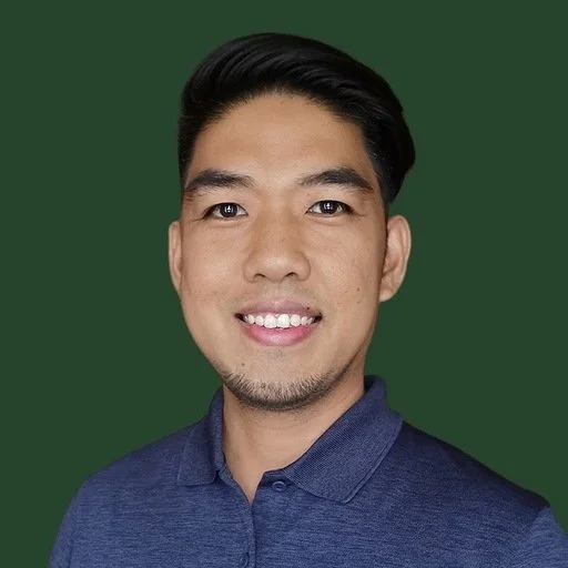 A young man with short black hair, light skin, wearing a blue collared shirt, smiling in front of a green background.