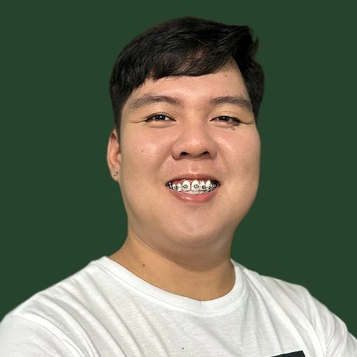 A young man with black hair smiling, wearing a white T-shirt, against a green background.