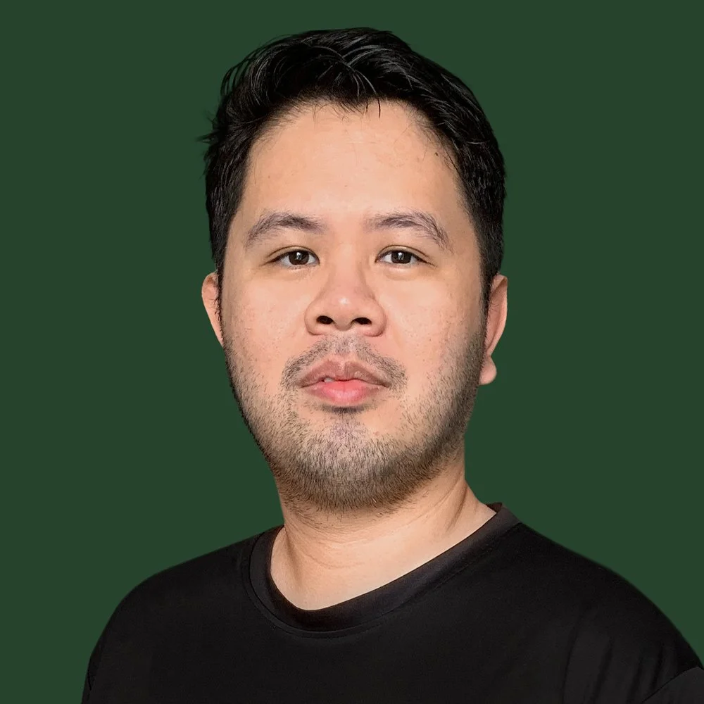 Portrait of a man with dark hair and a short beard, wearing a black shirt, against a green background.