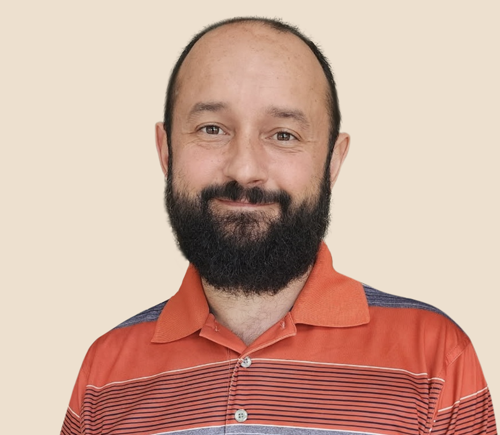 A man with light skin, a beard, and short hair, wearing an orange striped collared shirt, smiling against a plain beige background.