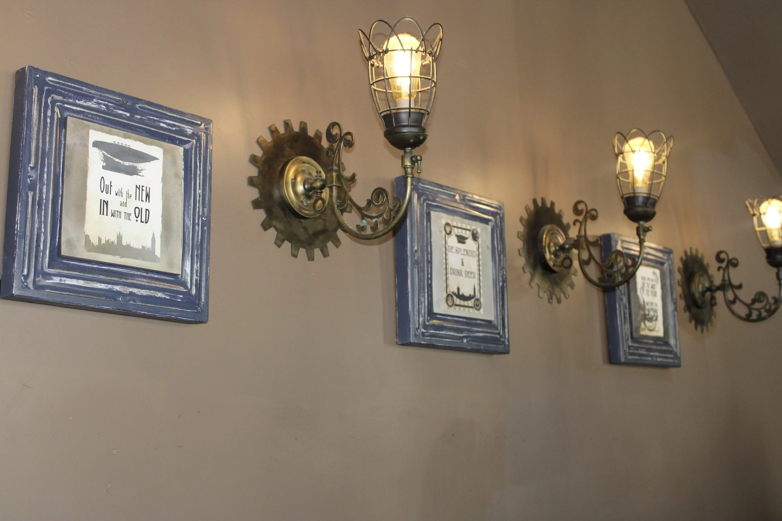 Decorative wall with framed quotes, metal gear wall accents, and vintage-style wall sconces with exposed bulbs.