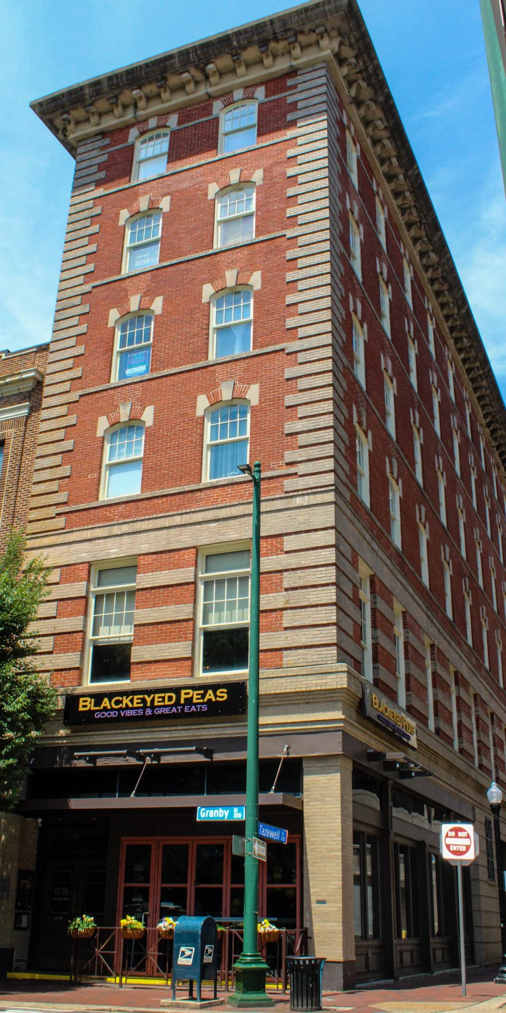 A multi-story brick building with large windows and a sign that reads "BlackEyed Peas Good Vibes & Great Eats." The building is located at the corner of a street with a green lamppost, street signs for Granby and Tazewell Streets, and a mailbox in fr