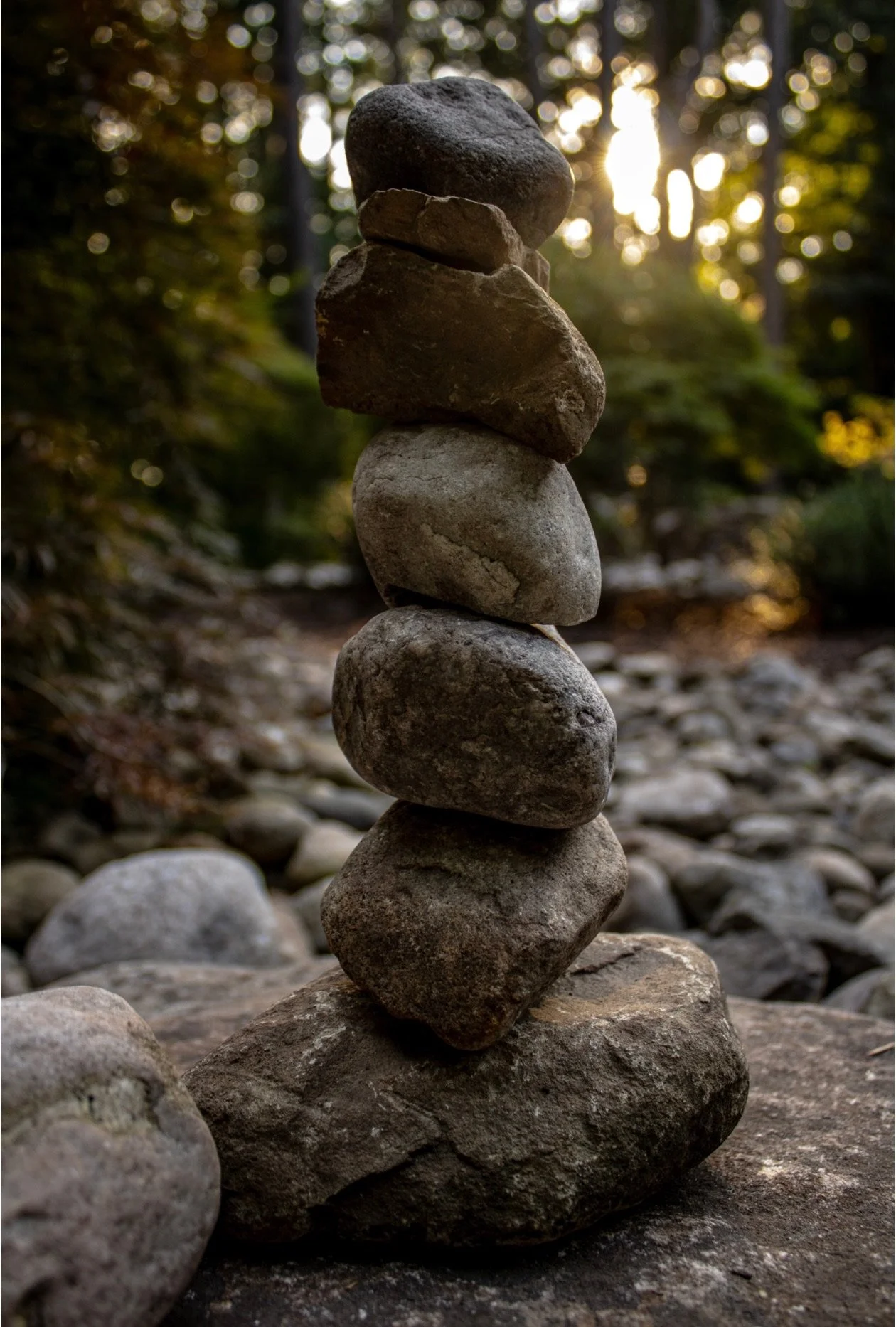 A balanced stack of rocks on a stone surface outdoors during sunset with trees and sunlight in the background.