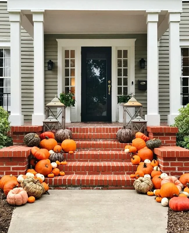Front porch decorated with numerous orange and white pumpkins and gourds on brick stairs and sidewalk.