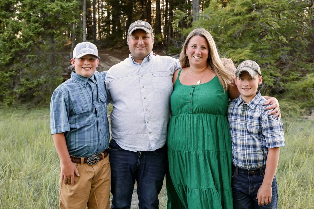 Verney Well Drilling family of four standing outdoors on a grassy trail in a wooded area, smiling at the camera.