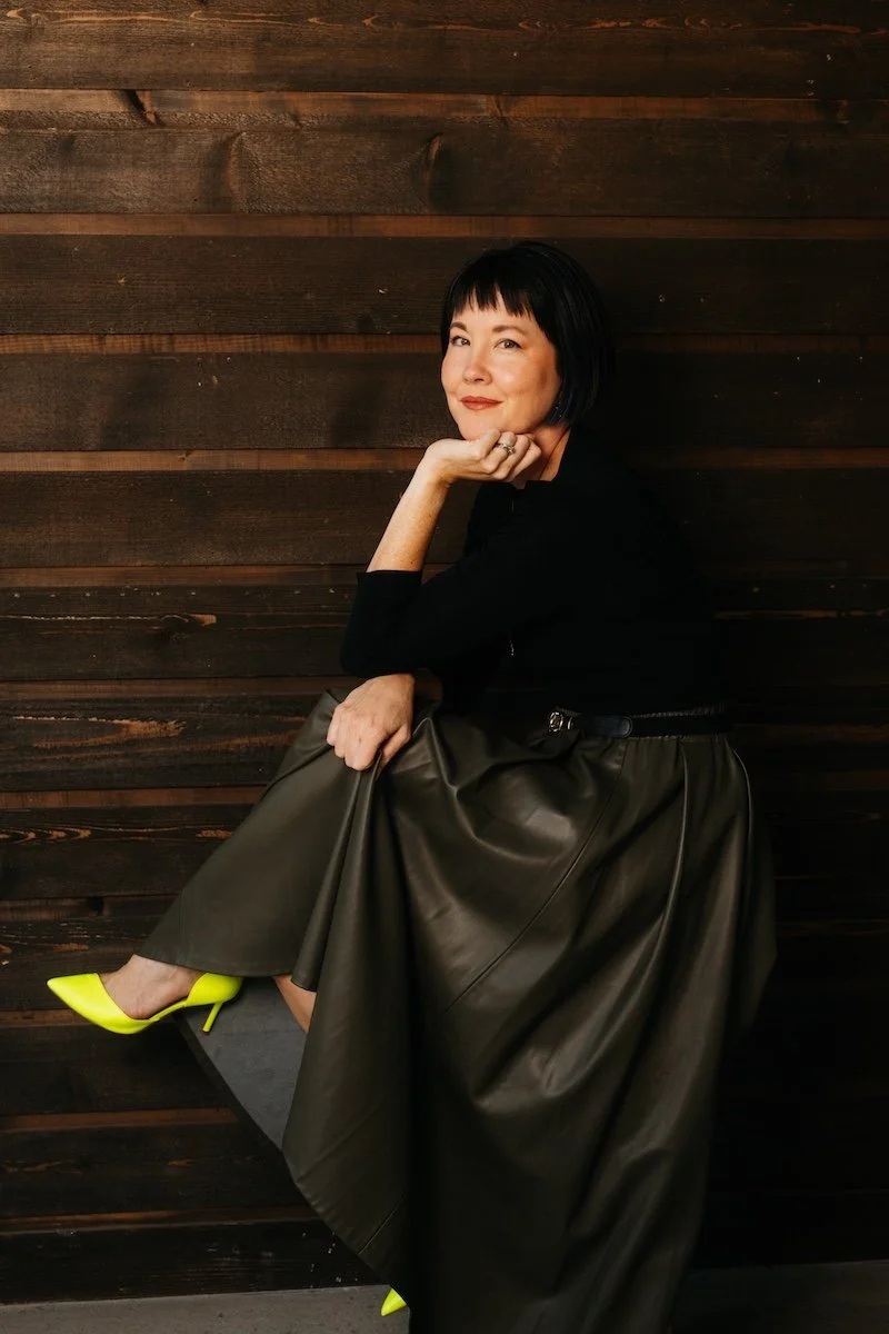 Photograph by Reed Schick of a woman sitting on in profile on a stool with neon yellow heels