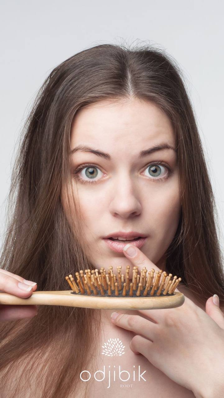 A woman with long brown hair holding a hairbrush with teeth near her face, looking surprised or curious.
