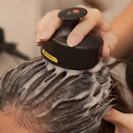 Person applying a hair treatment or shampoo to hair using a black device with a circular top.