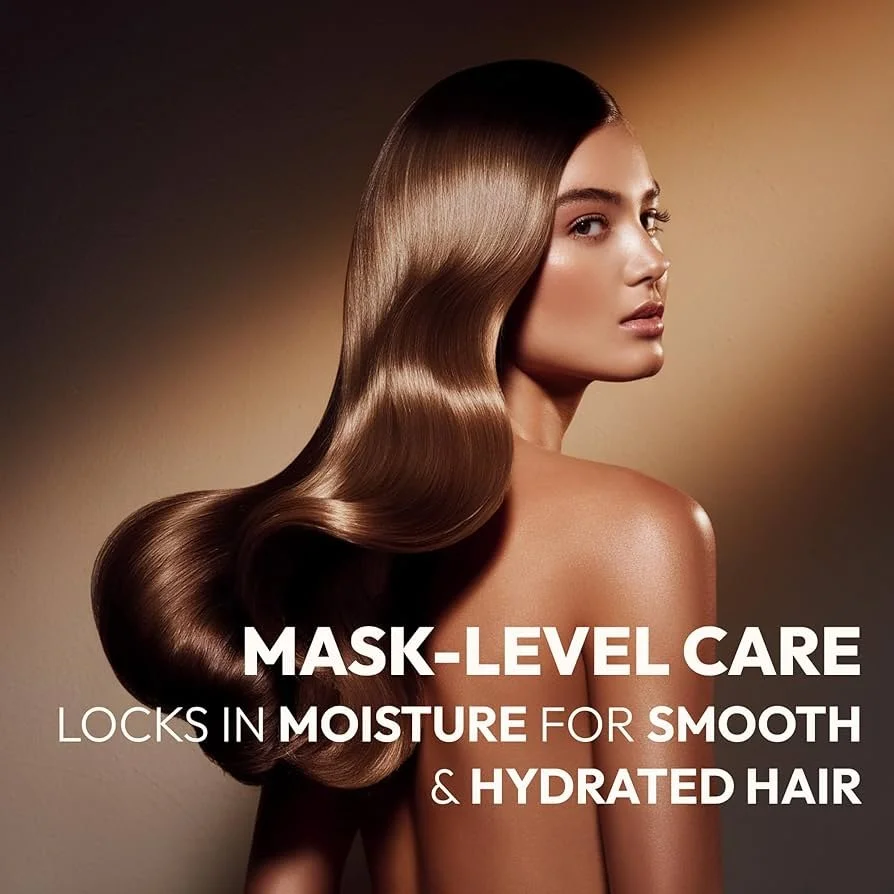 A woman with long, shiny, wavy brown hair posing topless with her shoulder exposed, advertising hair care for moisture and hydration.