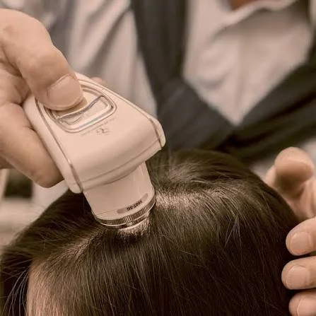 Person receiving a scalp treatment with a device, in a clinical setting.
