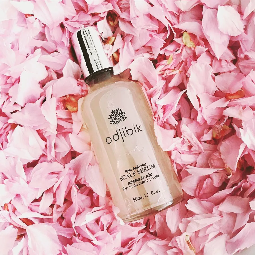 A bottle of Odjibik Root Activator Scalp Serum lying on pink rose petals.