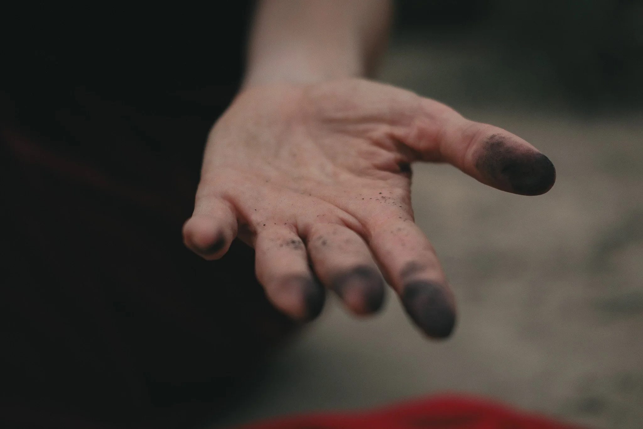 Close-up of a hand with blackened fingers from drawing with charcoal, held out against a blurred background.