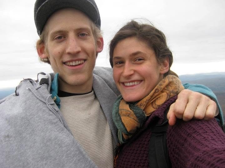 A smiling young man and woman taking a selfie outdoors on a cloudy day.