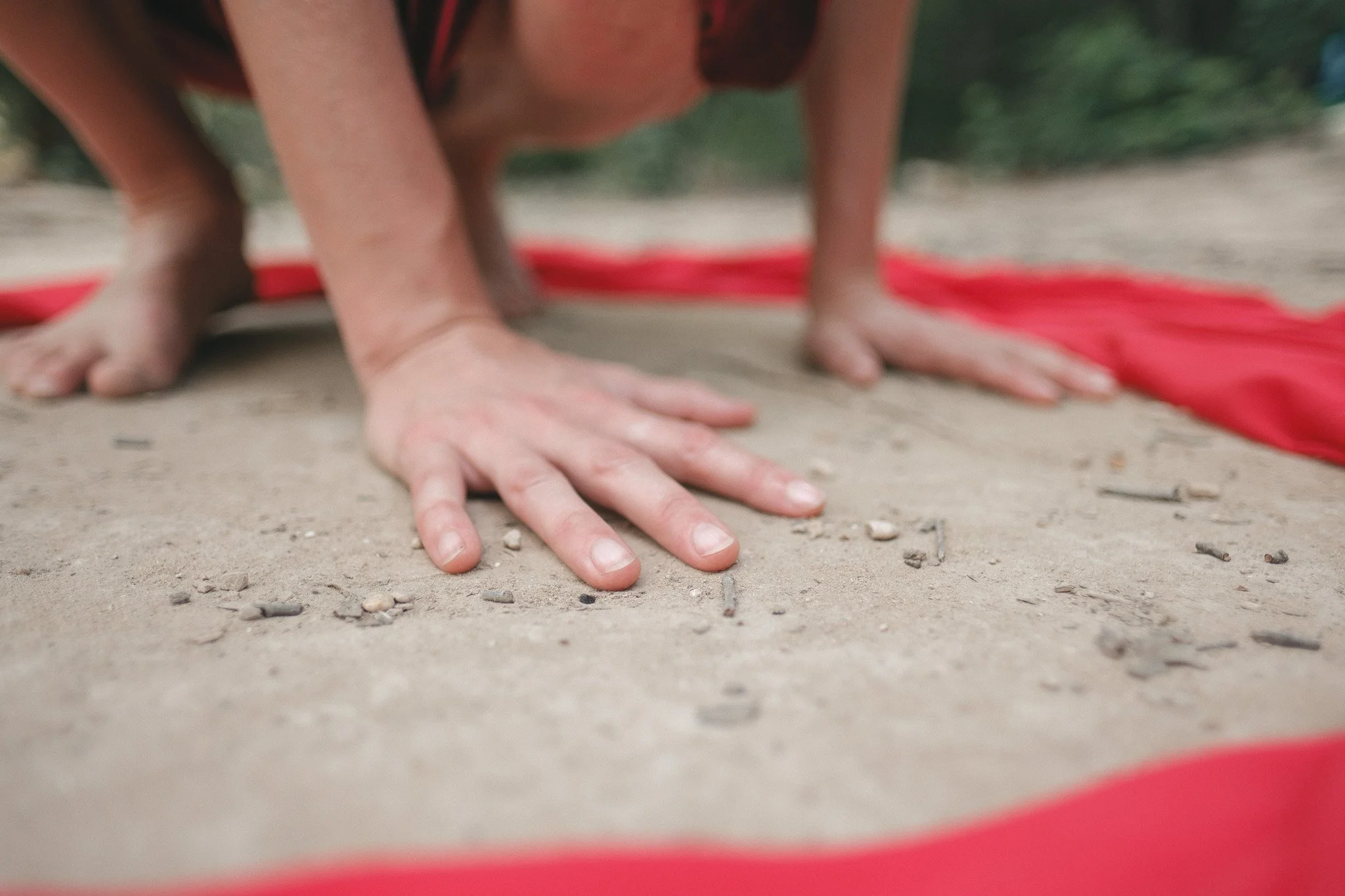 A woman inside a red circle of fabric squatting with her hands on the ground reverentially.